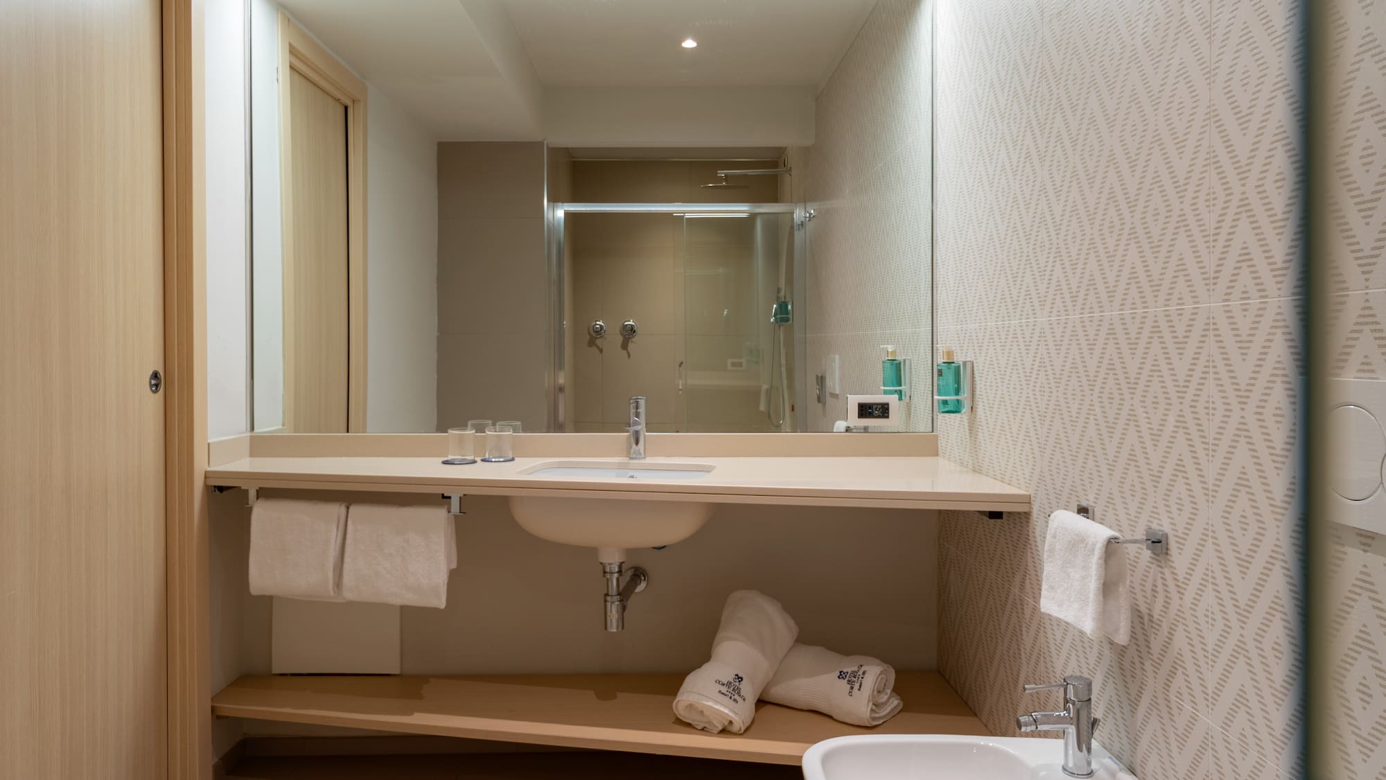 Modern hotel bathroom vanity, sink, mirror reflecting shower, bidet, and towels.