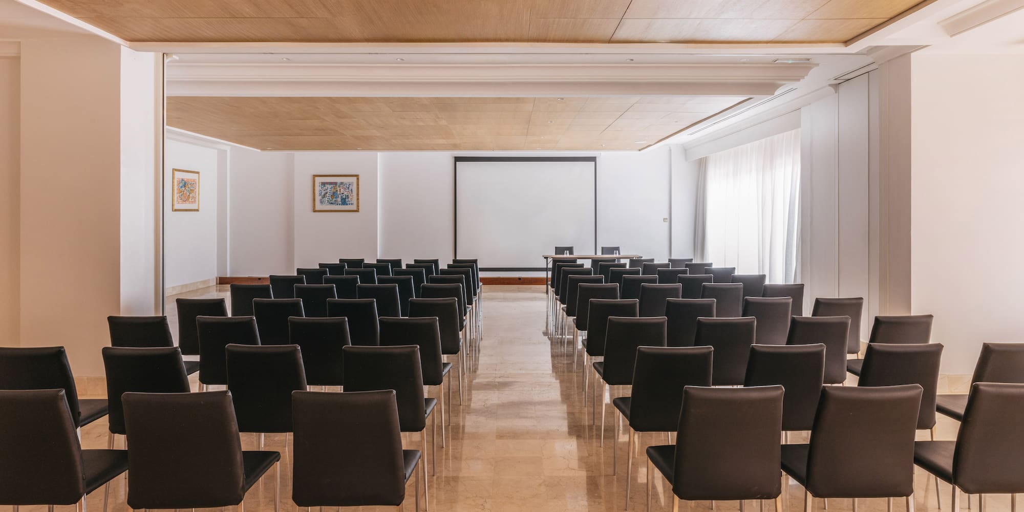 Spacious conference room with black chairs, projector screen, and wood ceiling.