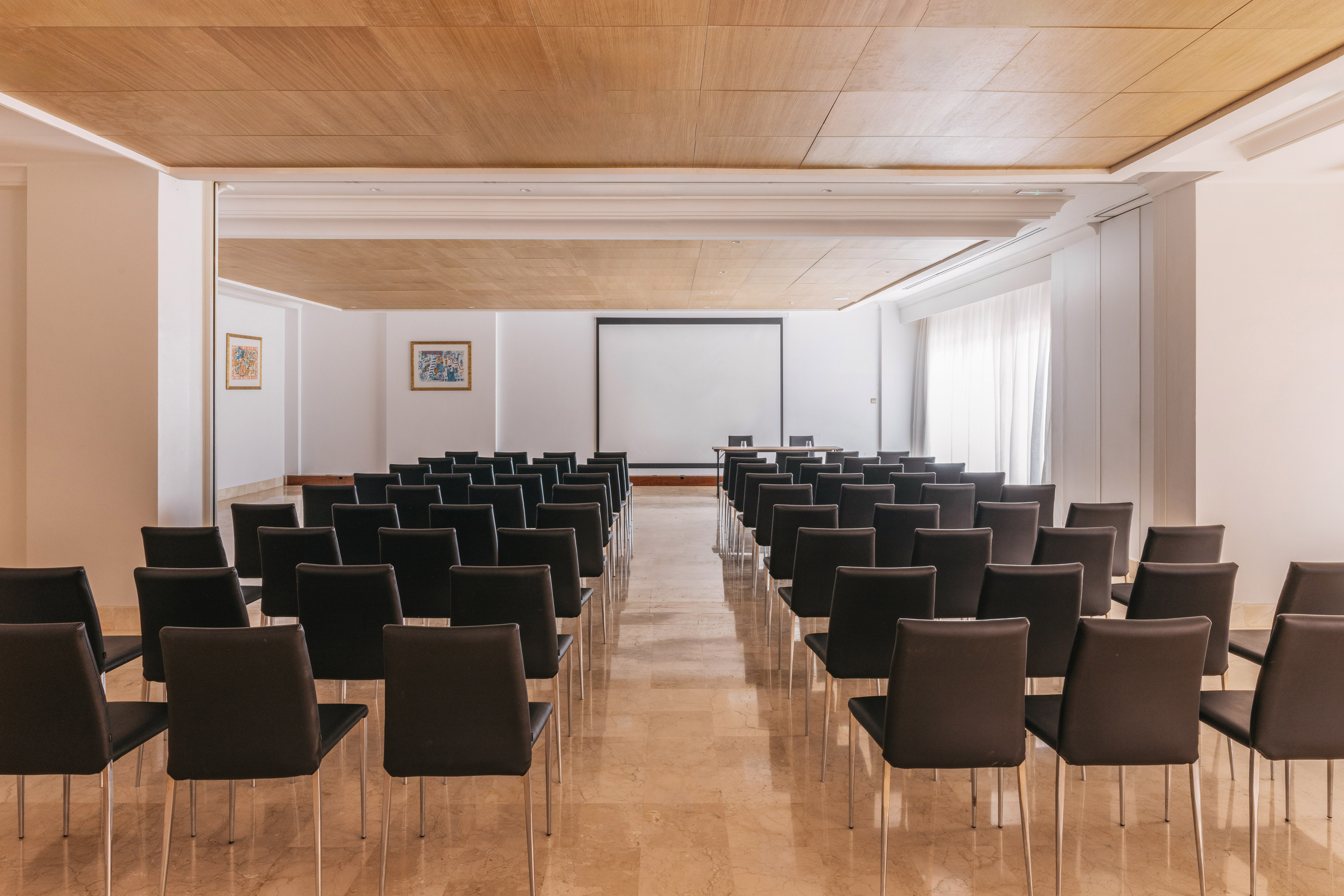 Spacious conference room with black chairs, projector screen, and wood ceiling.