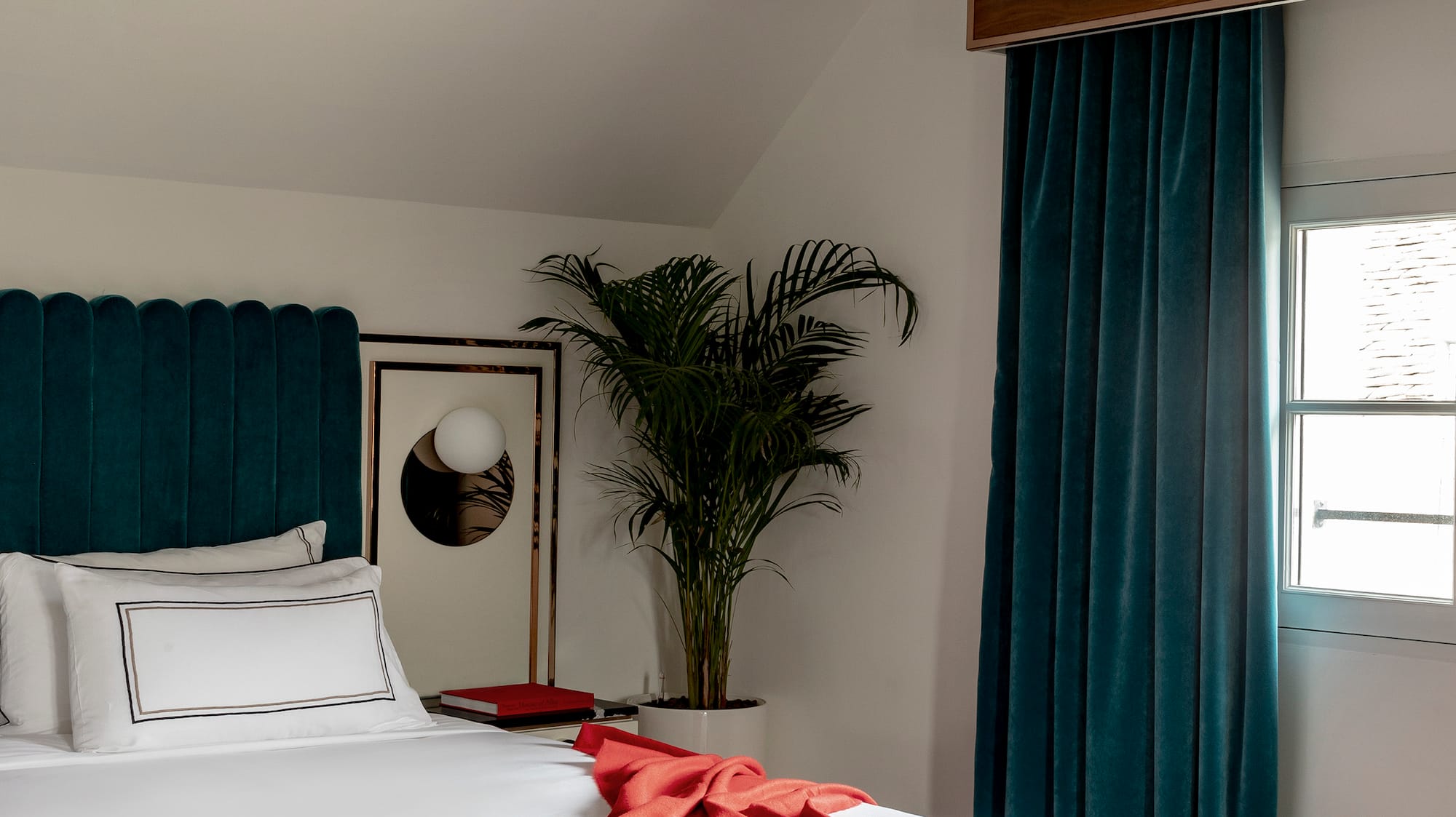 a bed with a red blanket and a palm tree in a room