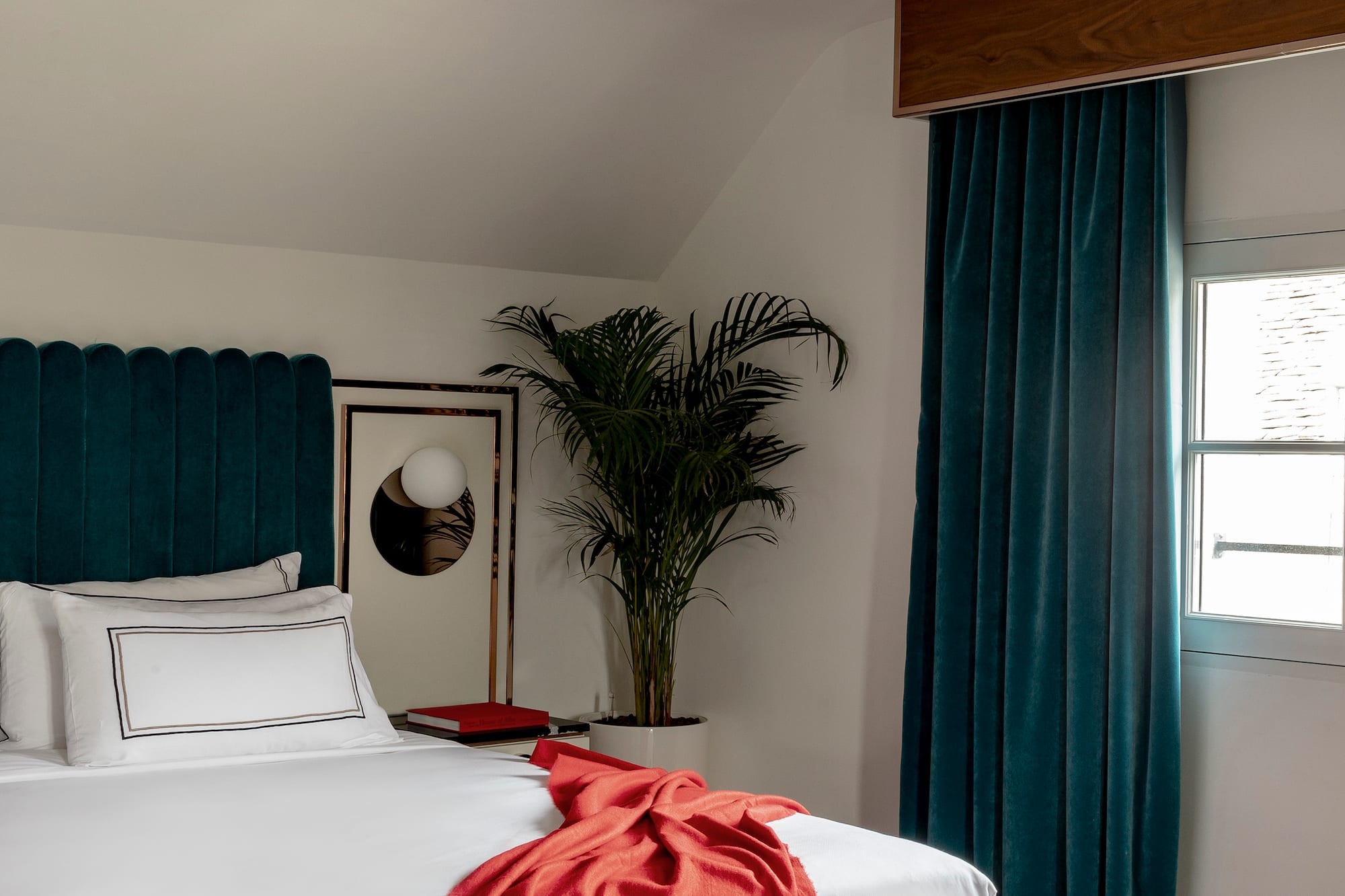 a bed with a red blanket and a palm tree in a room