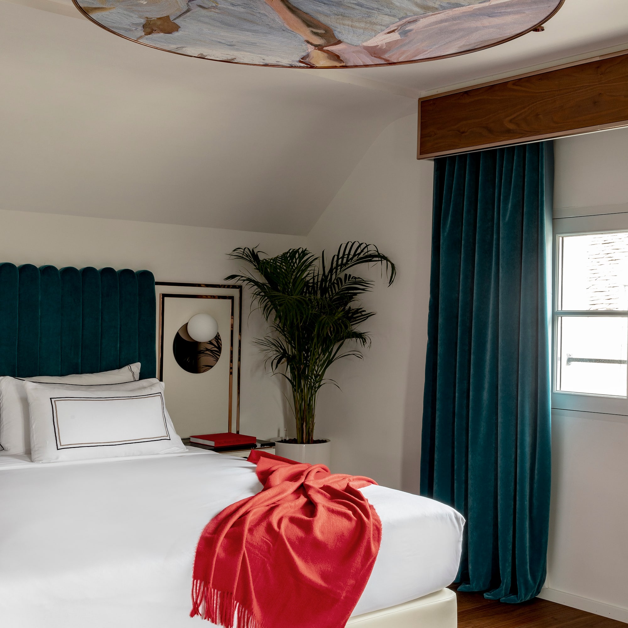 a bed with a red blanket and a palm tree in a room