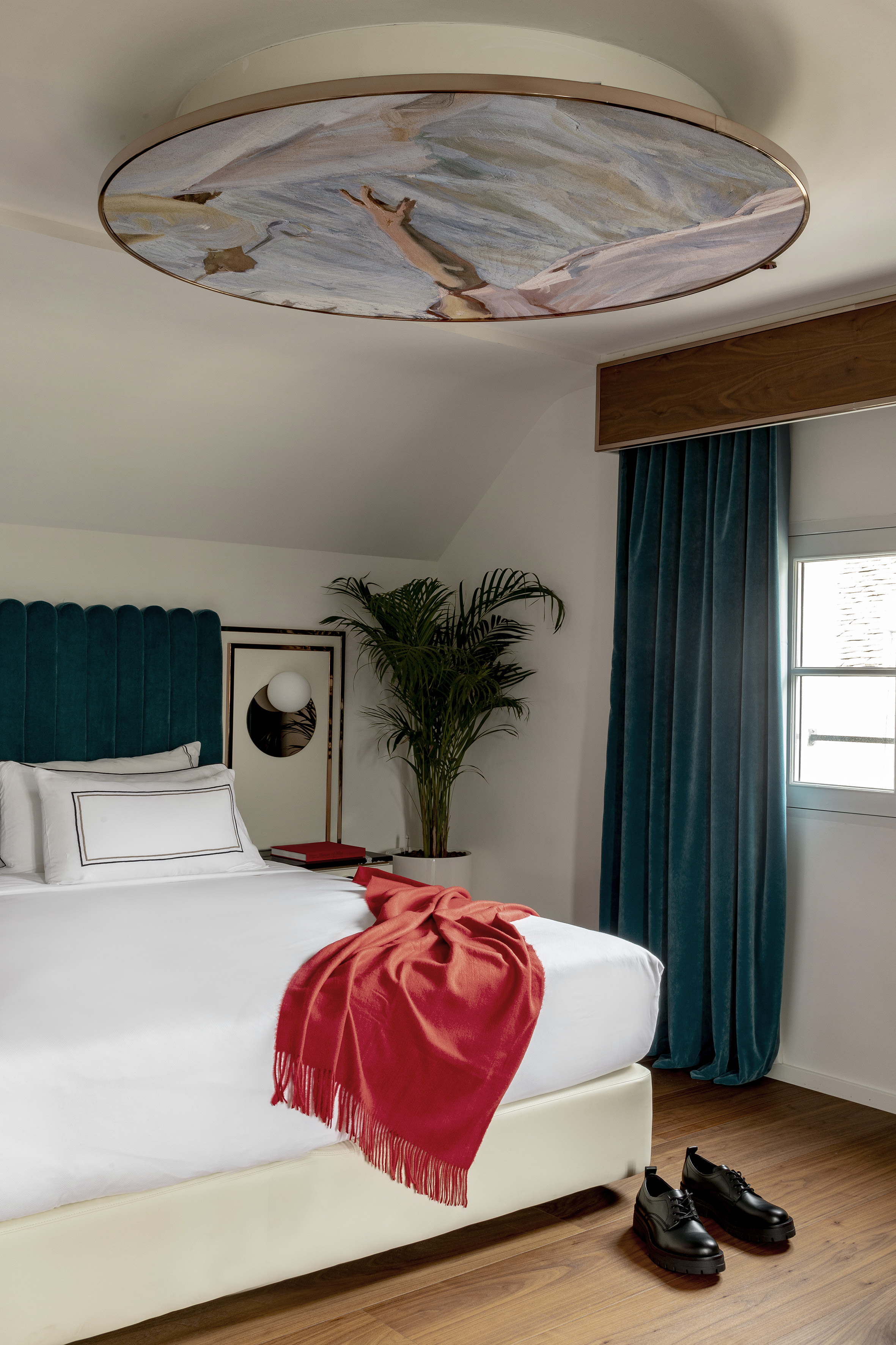 Modern bedroom with teal headboard, white bed, red throw, and artistic ceiling light.