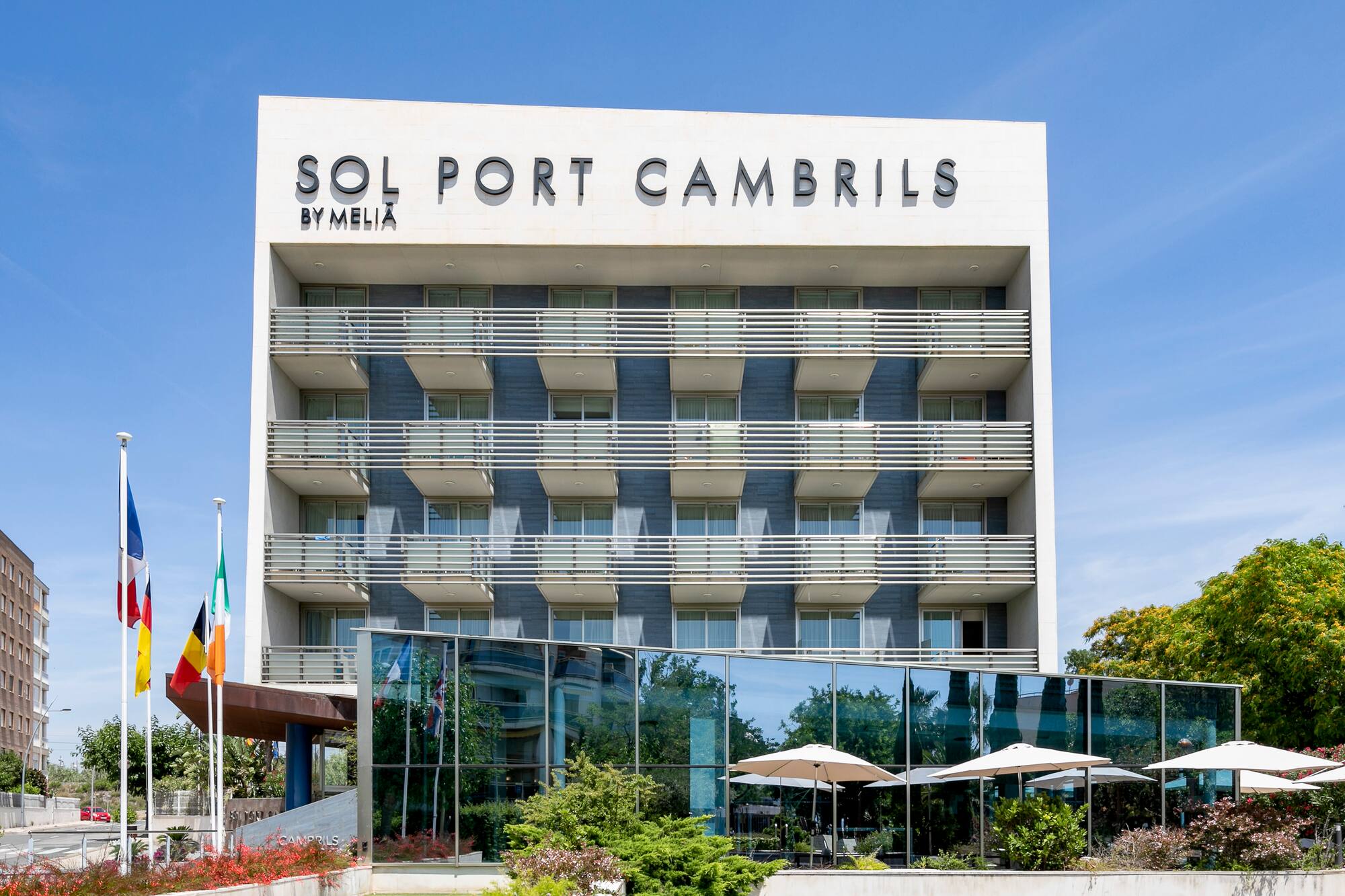 Sol Port Cambrils by Meliá hotel exterior with flags and balconies under blue sky.