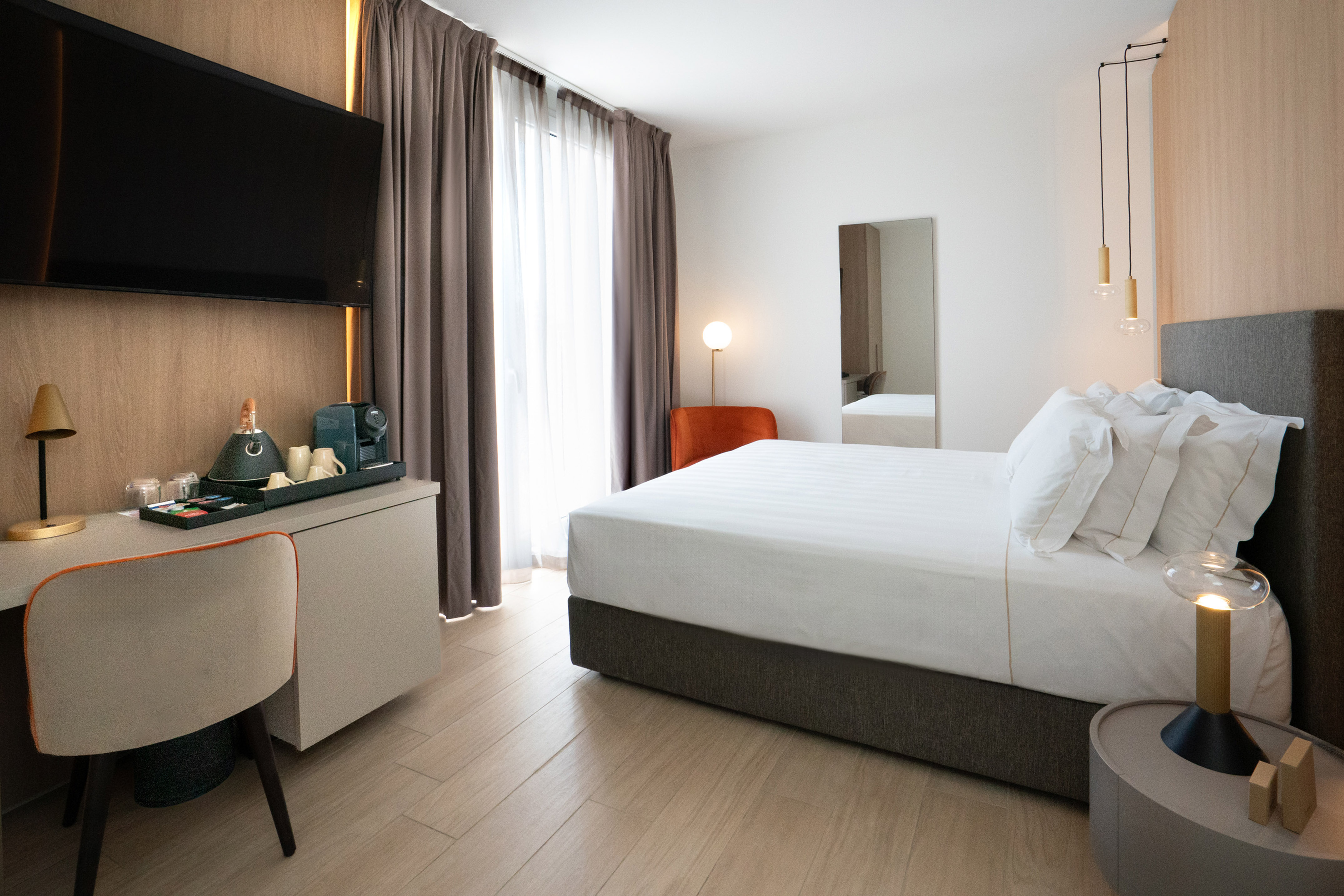 Modern hotel room with bed, workspace, TV, and coffee amenities.