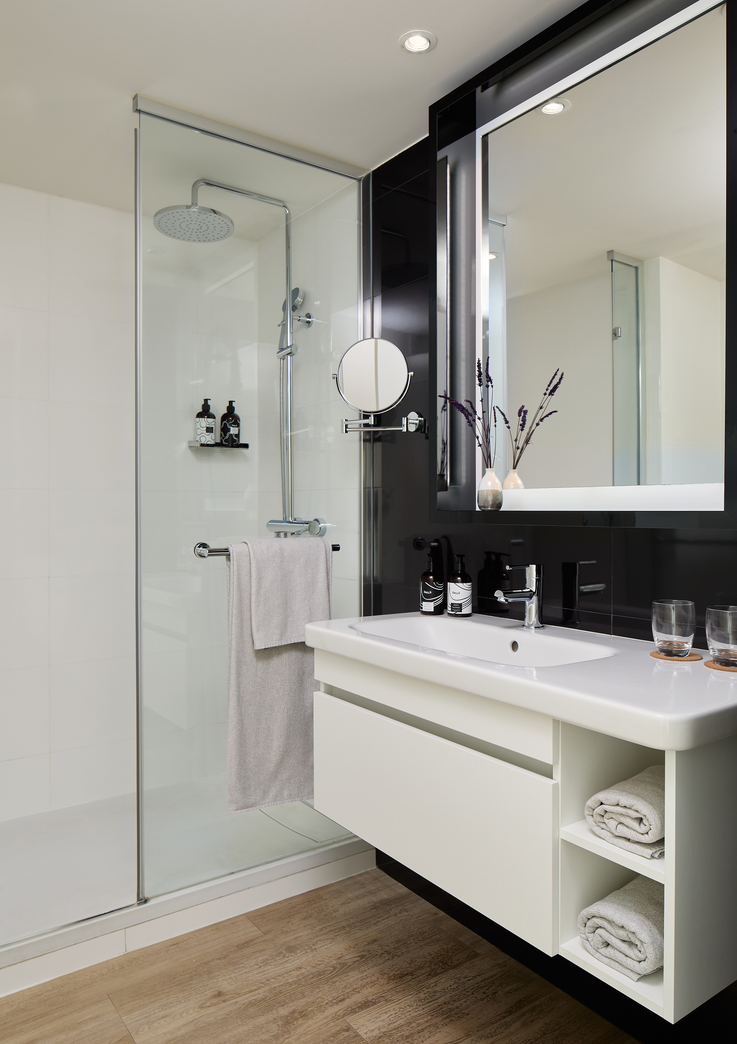 Modern bathroom with glass shower, white vanity, black wall, and mirror.