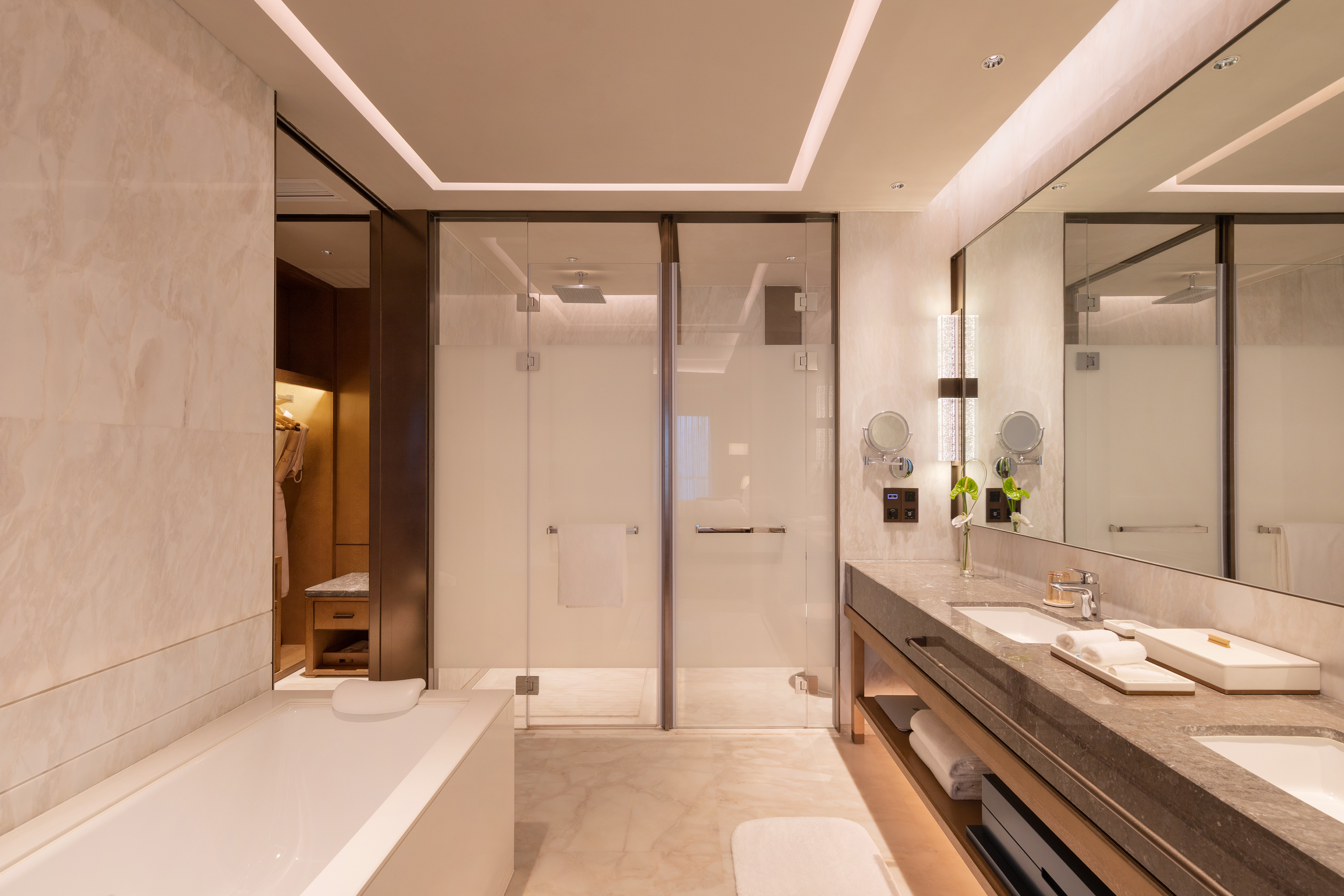 Luxury hotel bathroom with marble vanity, soaking tub, and glass shower.