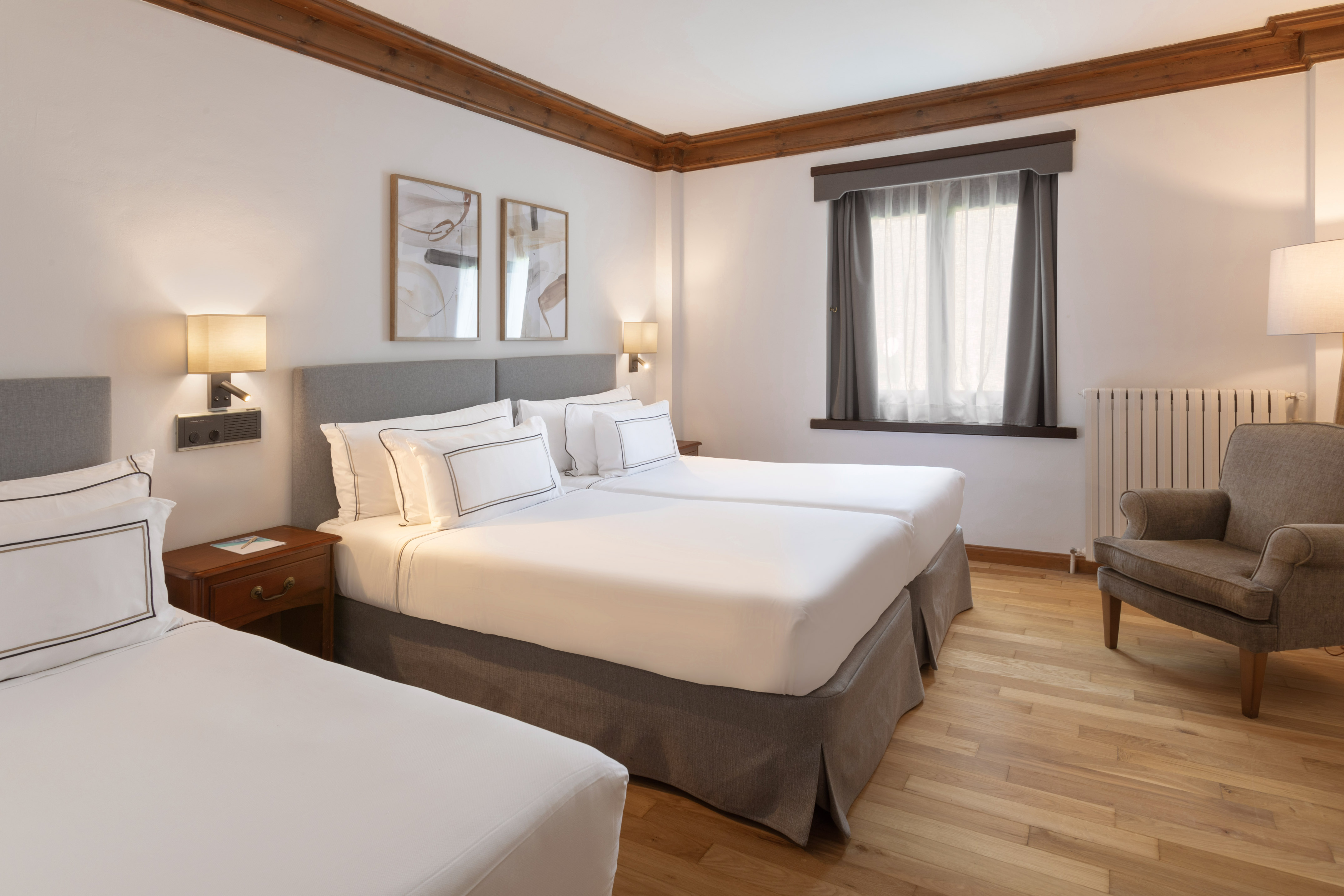 Bright triple hotel room with two twin beds, single bed, wood floor, and armchair.