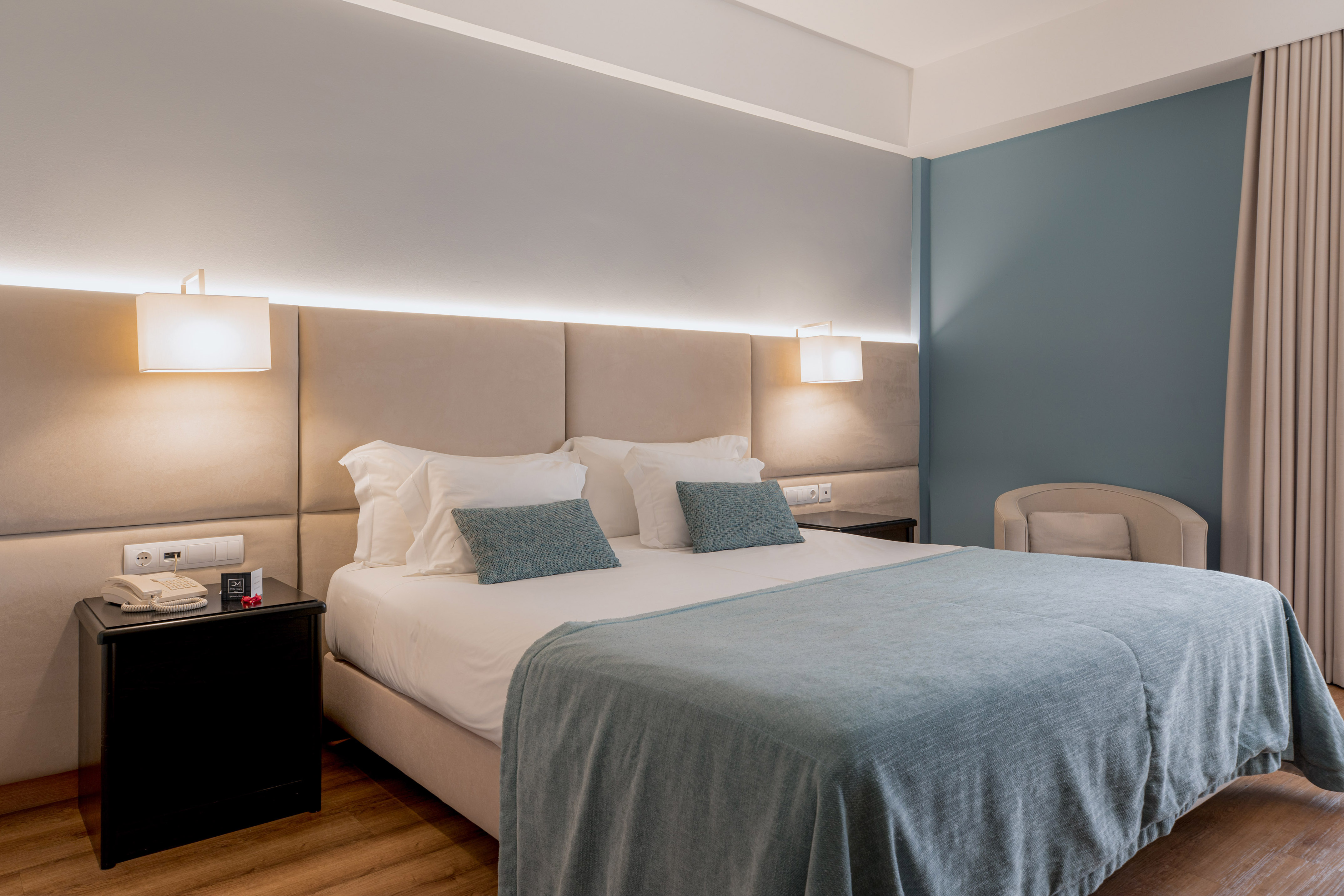 Modern hotel bedroom with cozy king-size bed, blue accents, and warm lighting.