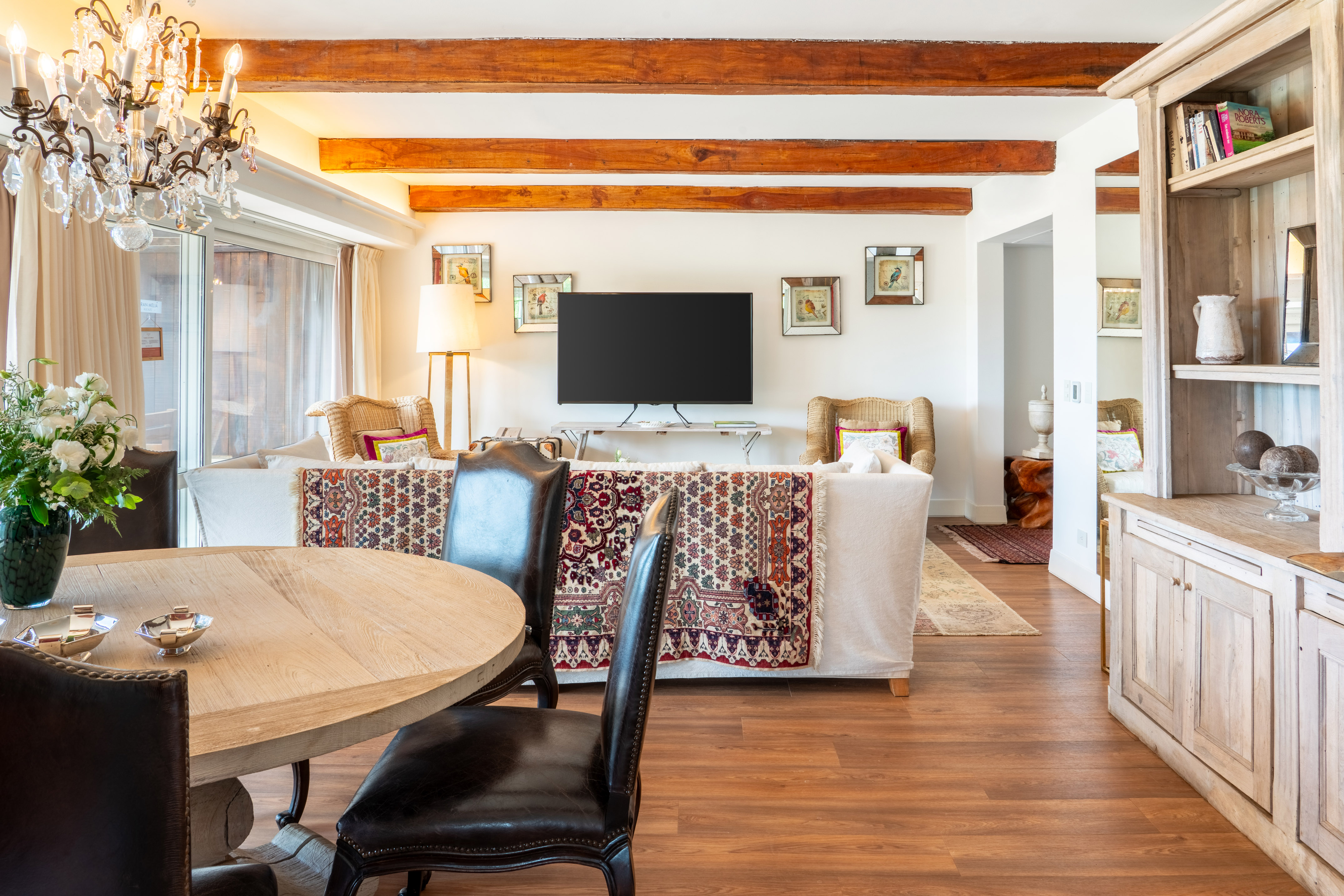 Living room with wood beams, chandelier, sofa, TV, and dining table.