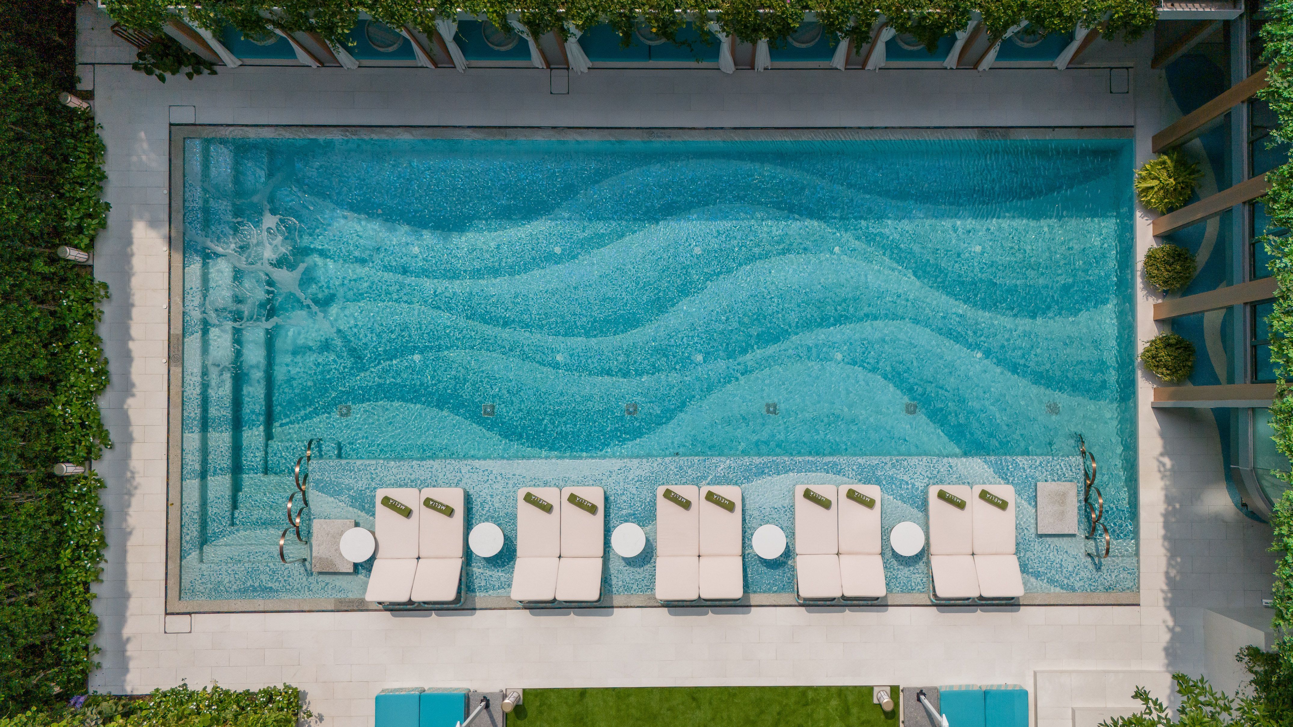 Overhead luxury pool with wave mosaic tiles and Melia lounge chairs.