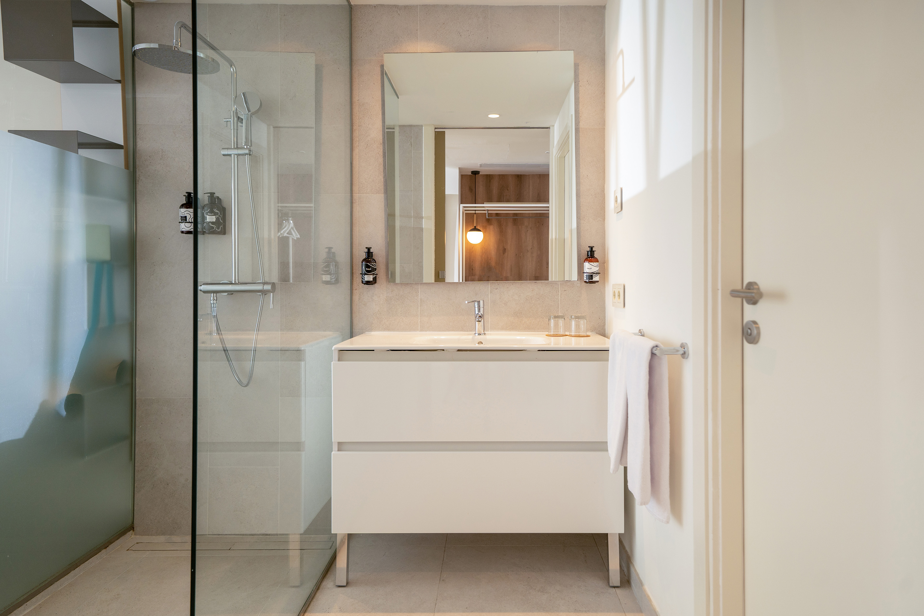 Sleek hotel bathroom featuring a glass shower, white vanity, and large mirror.