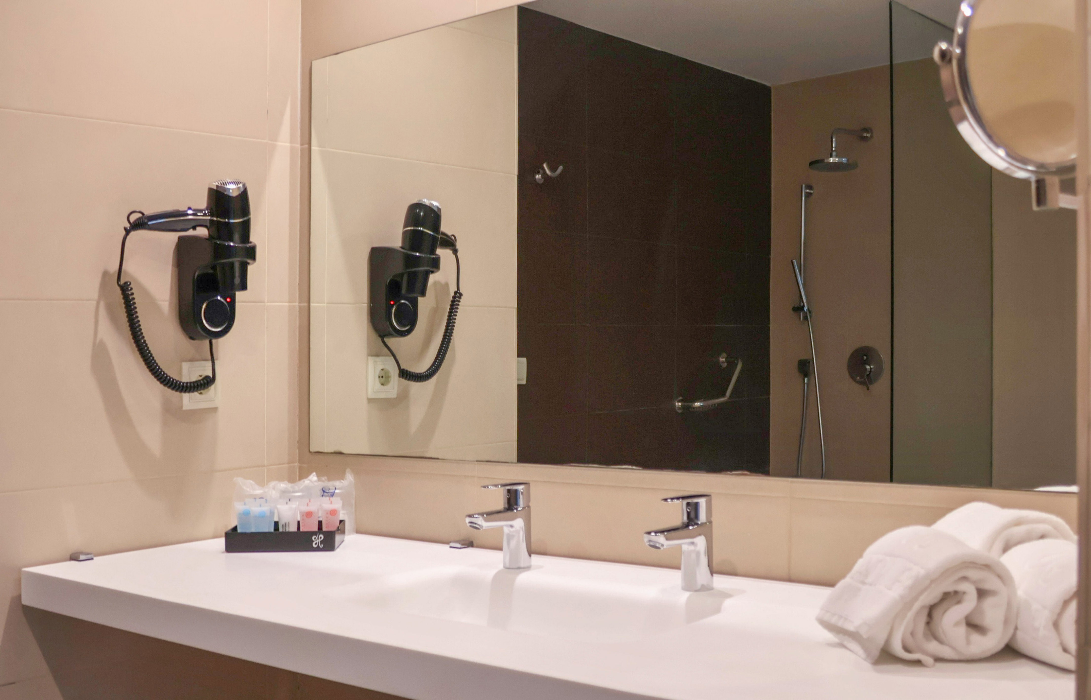 Modern bathroom with double vanity, mirror, wall-mounted hairdryer, and shower.