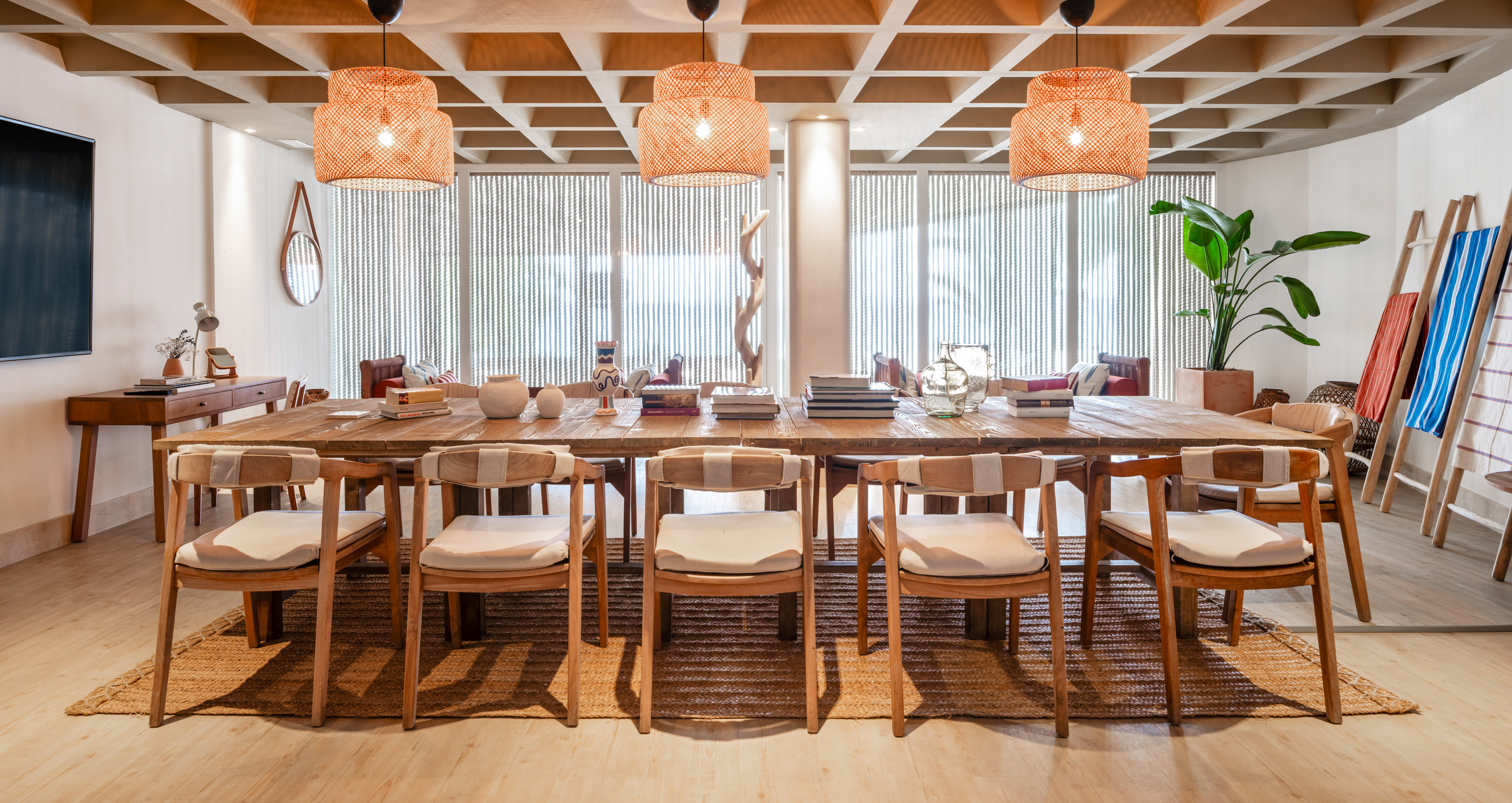 Long wooden dining table with chairs, rattan pendant lights, and natural room decor.