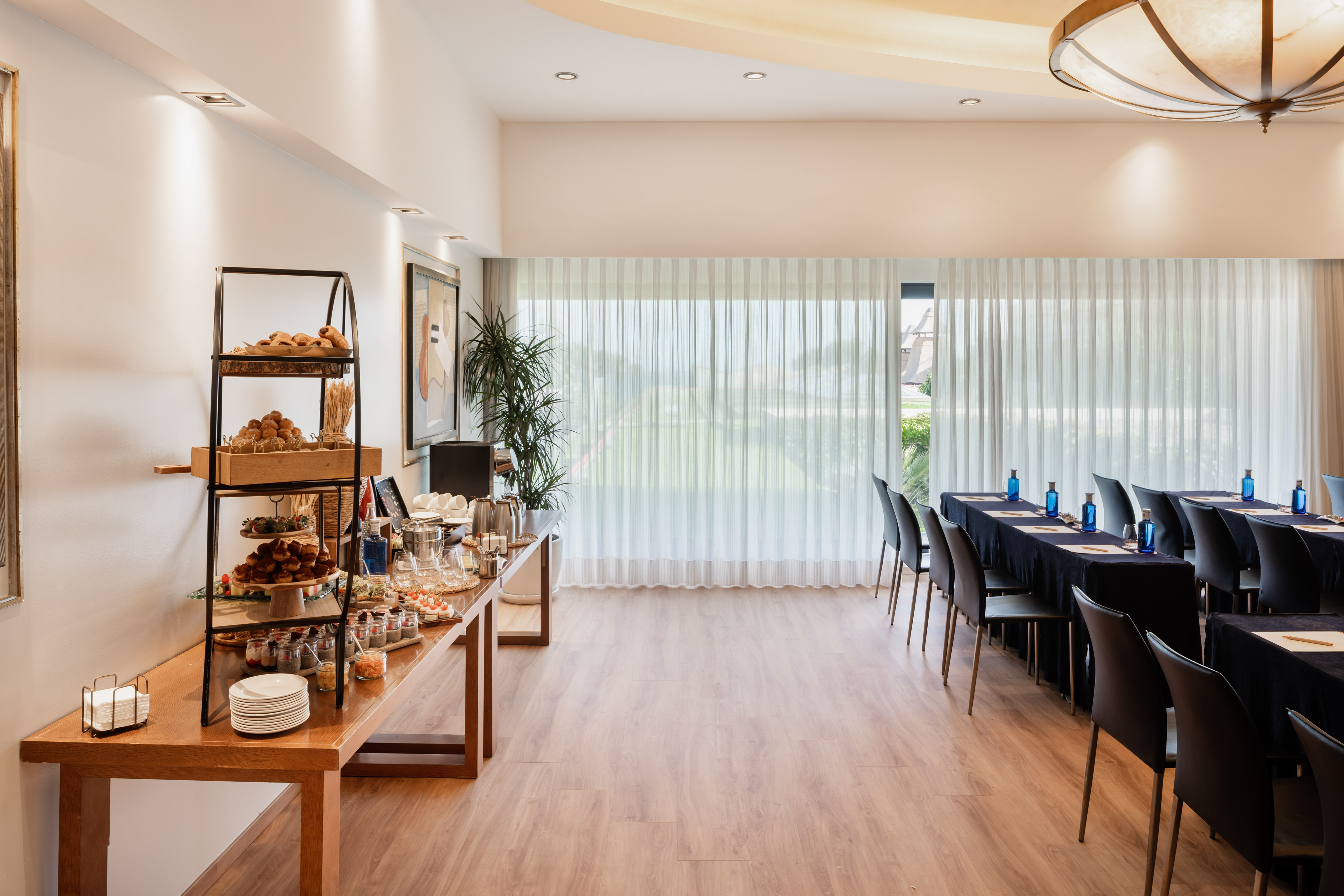 Hotel conference room with catering buffet, dark tables, and bright windows.