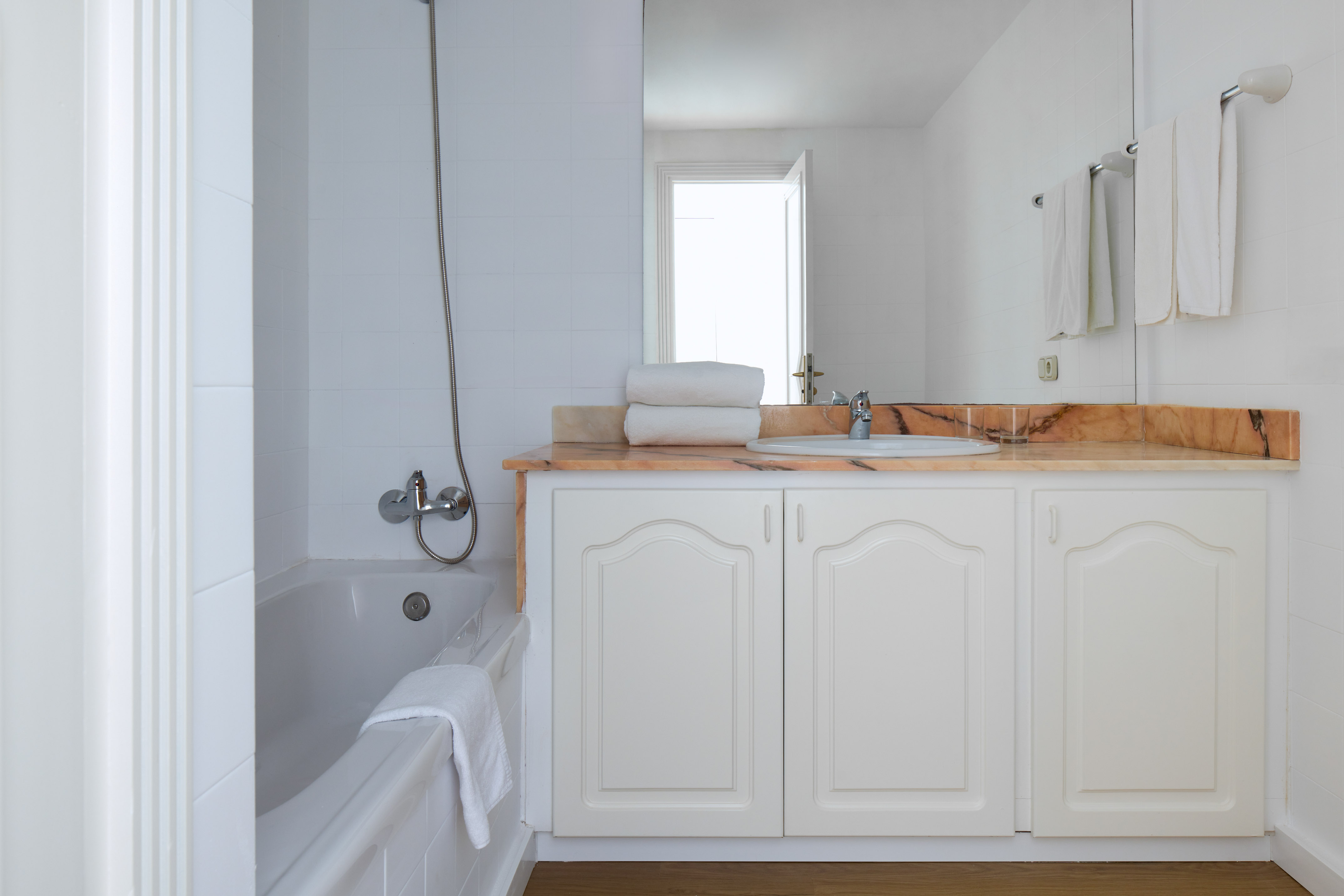 White tiled bathroom with bathtub, marble vanity, sink, and fresh towels.