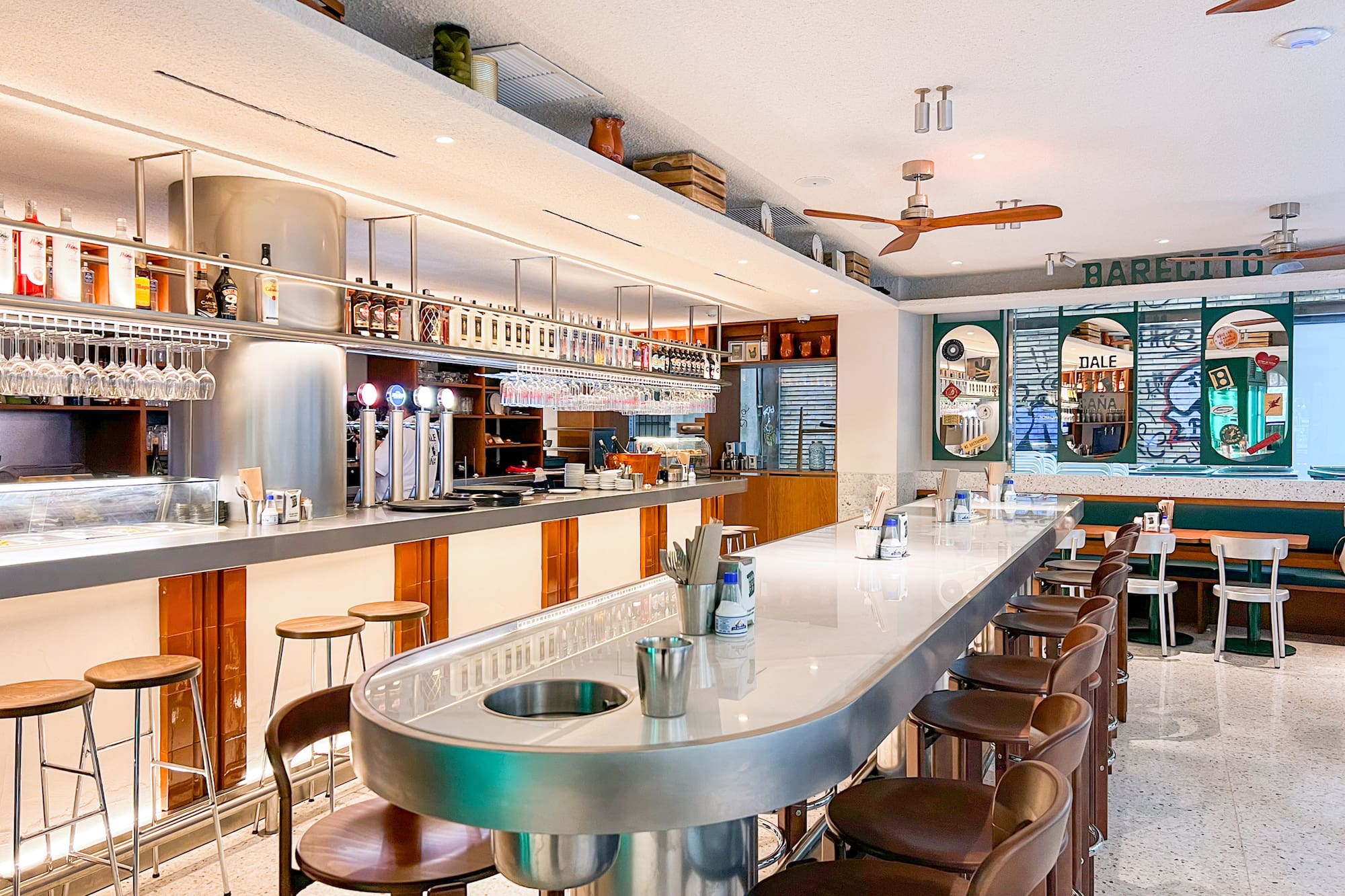Bright, modern bar interior with long counter, bar stools, and liquor display.