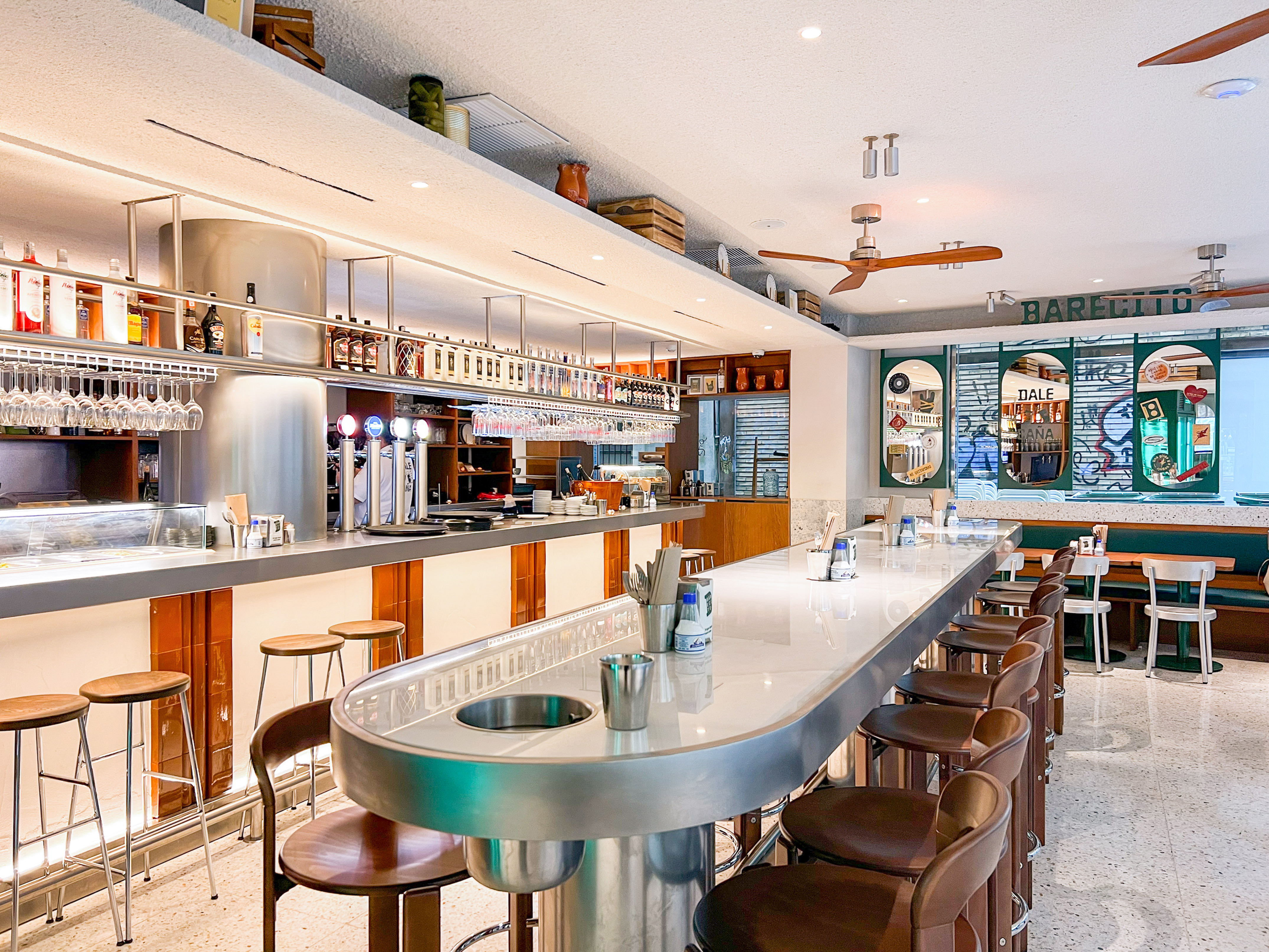 Bright, modern bar interior with long counter, bar stools, and liquor display.