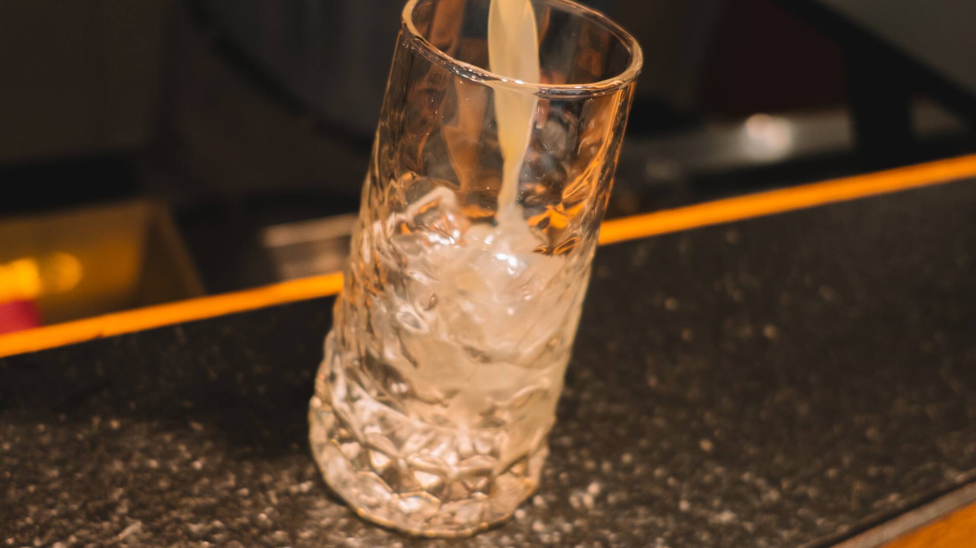 Bartender pouring cocktail from jigger into iced glass.