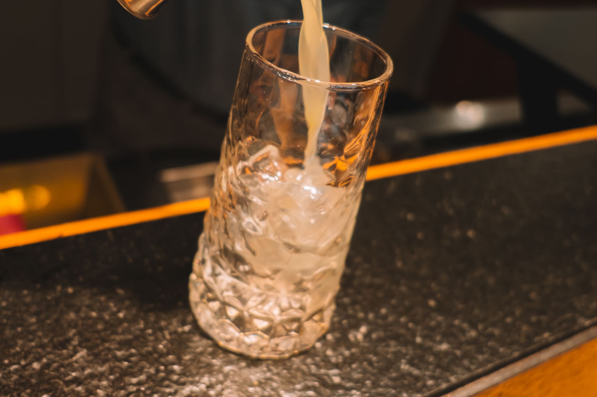 Bartender pouring cocktail from jigger into iced glass.