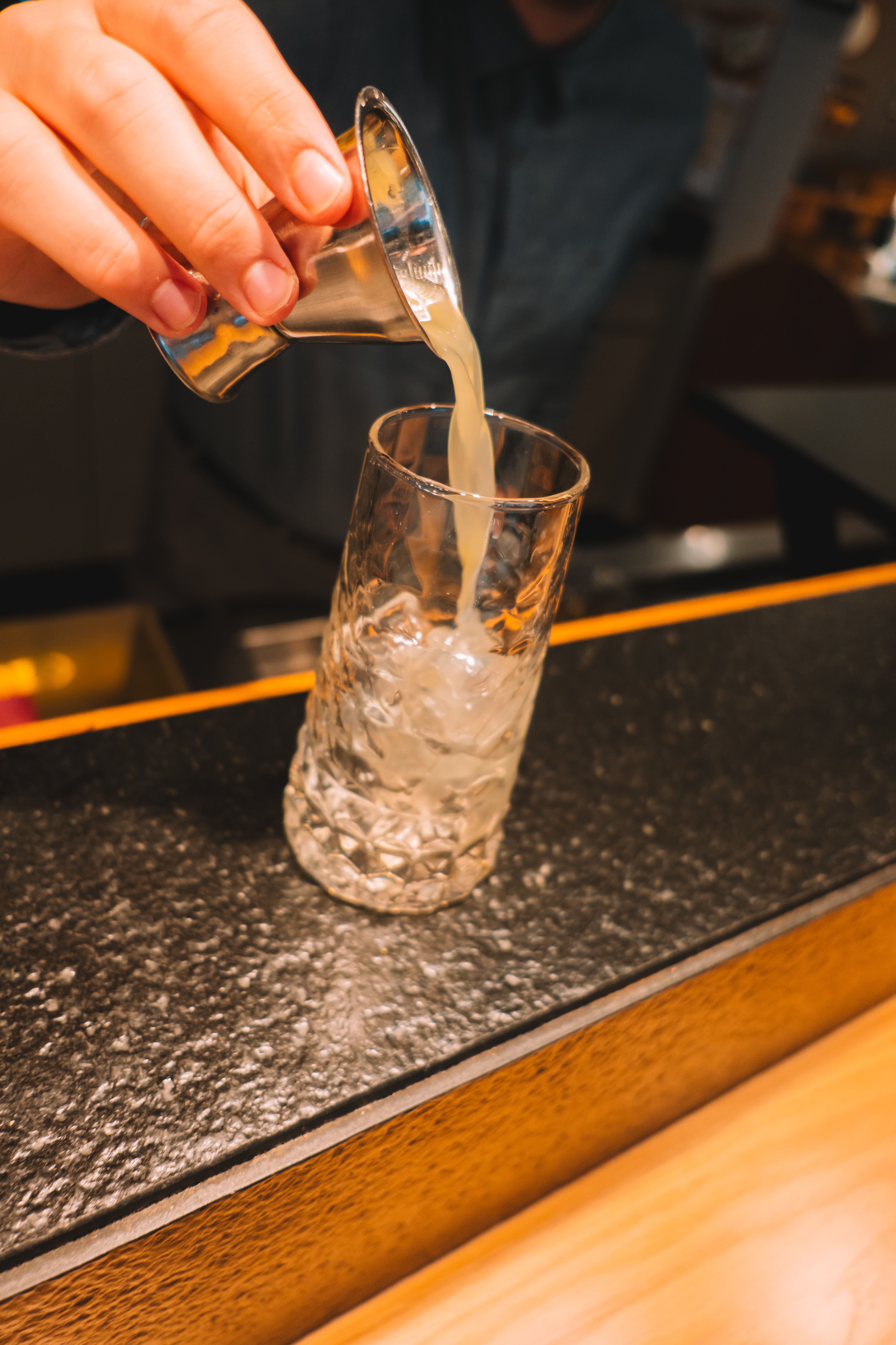 Bartender pouring cocktail from jigger into iced glass.