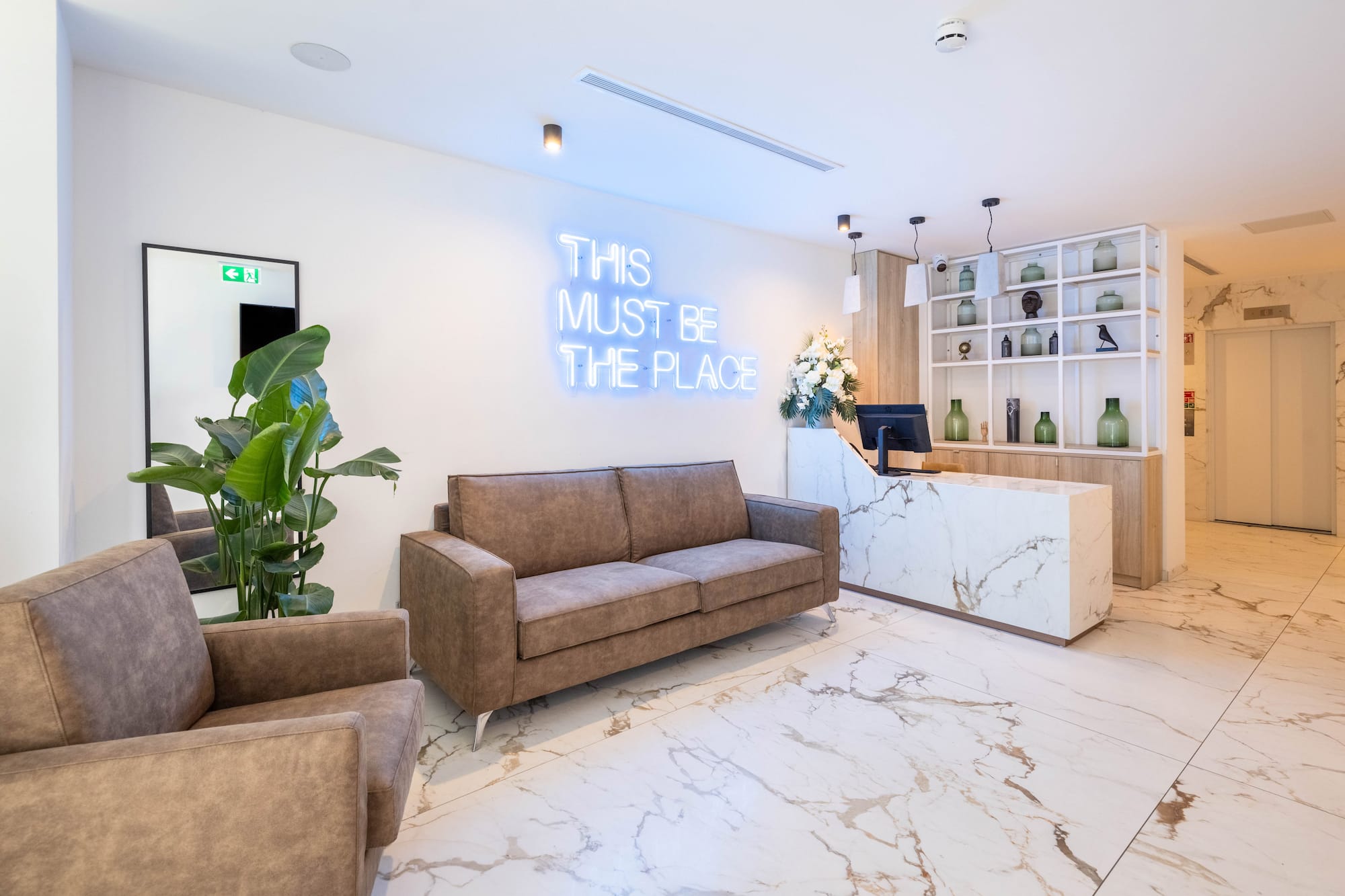 Modern hotel lobby with neon sign, marble floor, brown sofas, and reception desk.