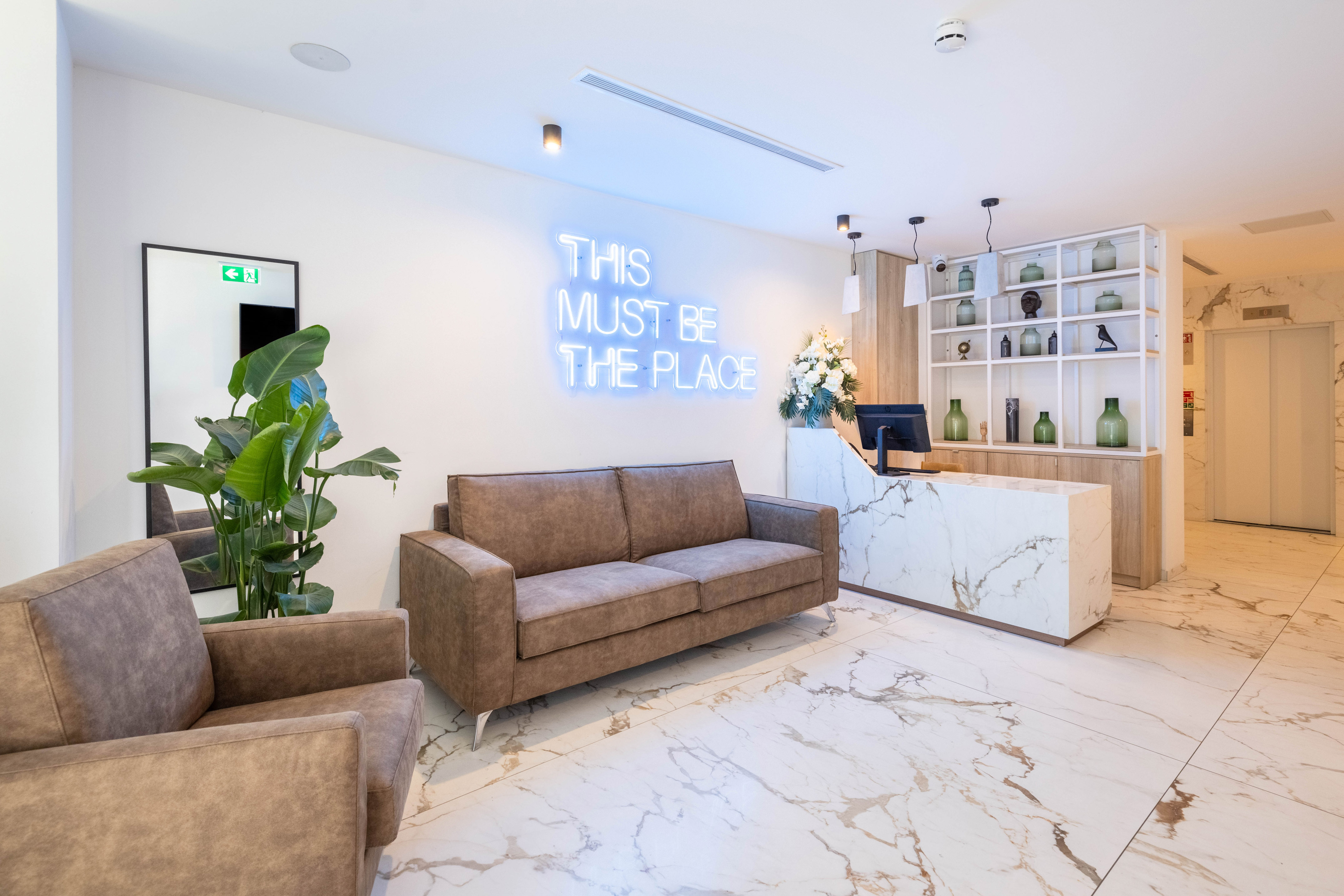 Modern hotel lobby with neon sign, marble floor, brown sofas, and reception desk.