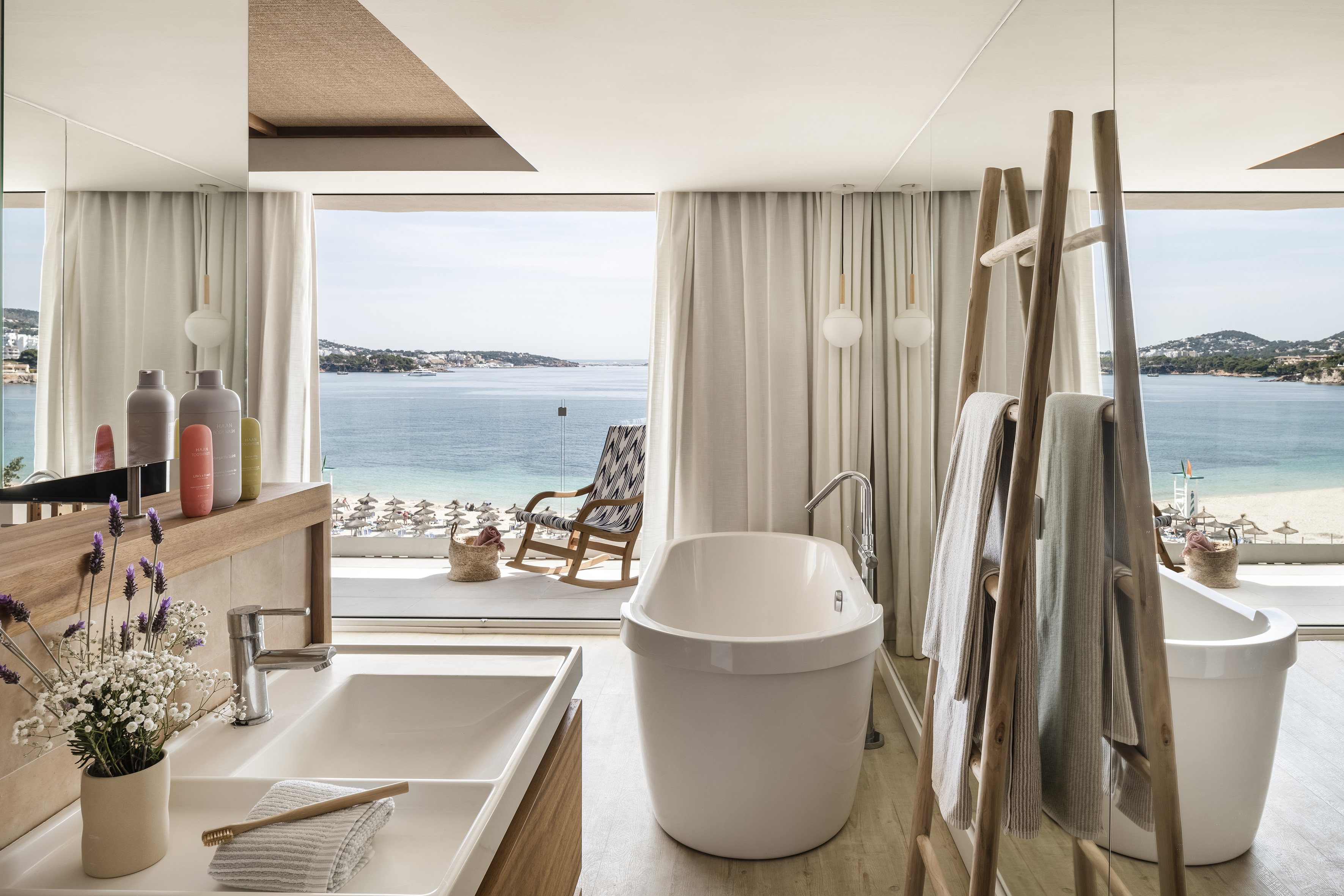 Luxury hotel bathroom with ocean view, beach, modern bathtub, and vanity.
