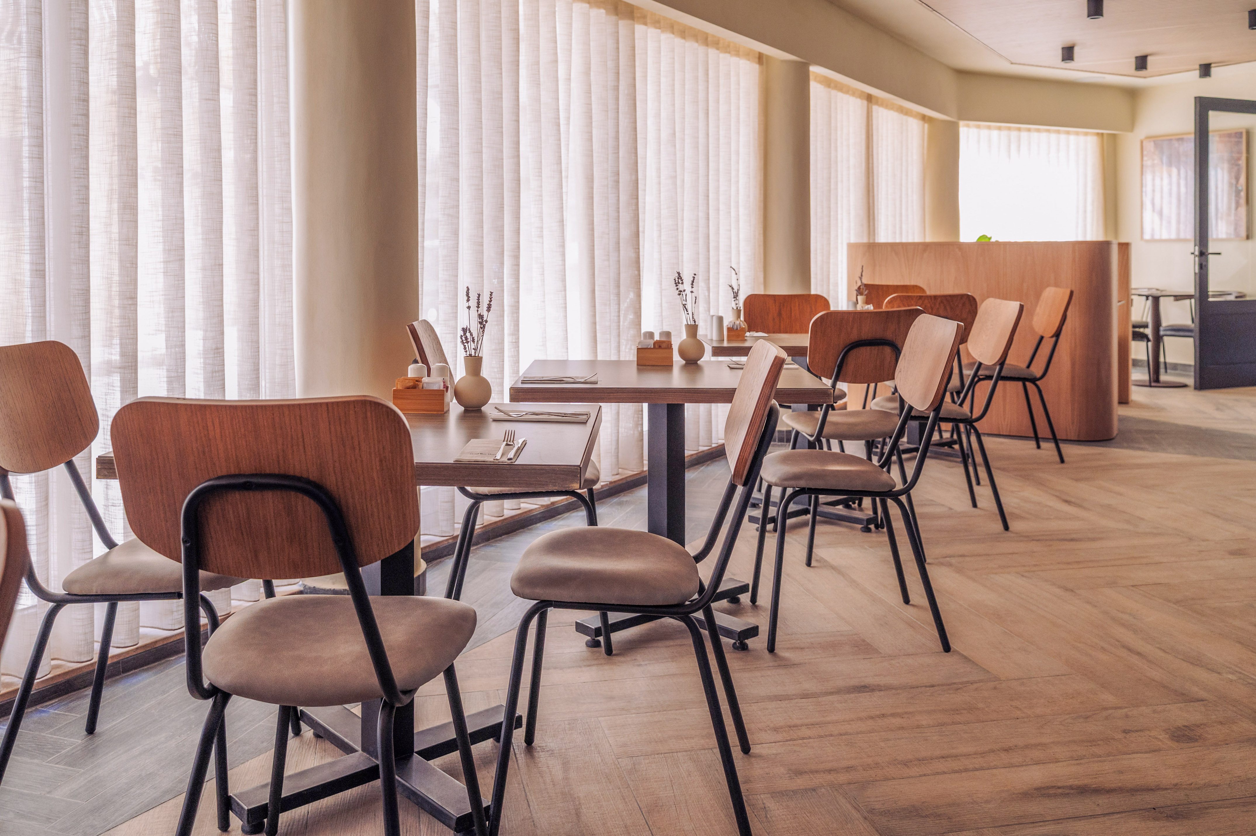 Modern cafe dining space with wooden tables, minimalist chairs, sheer curtains.