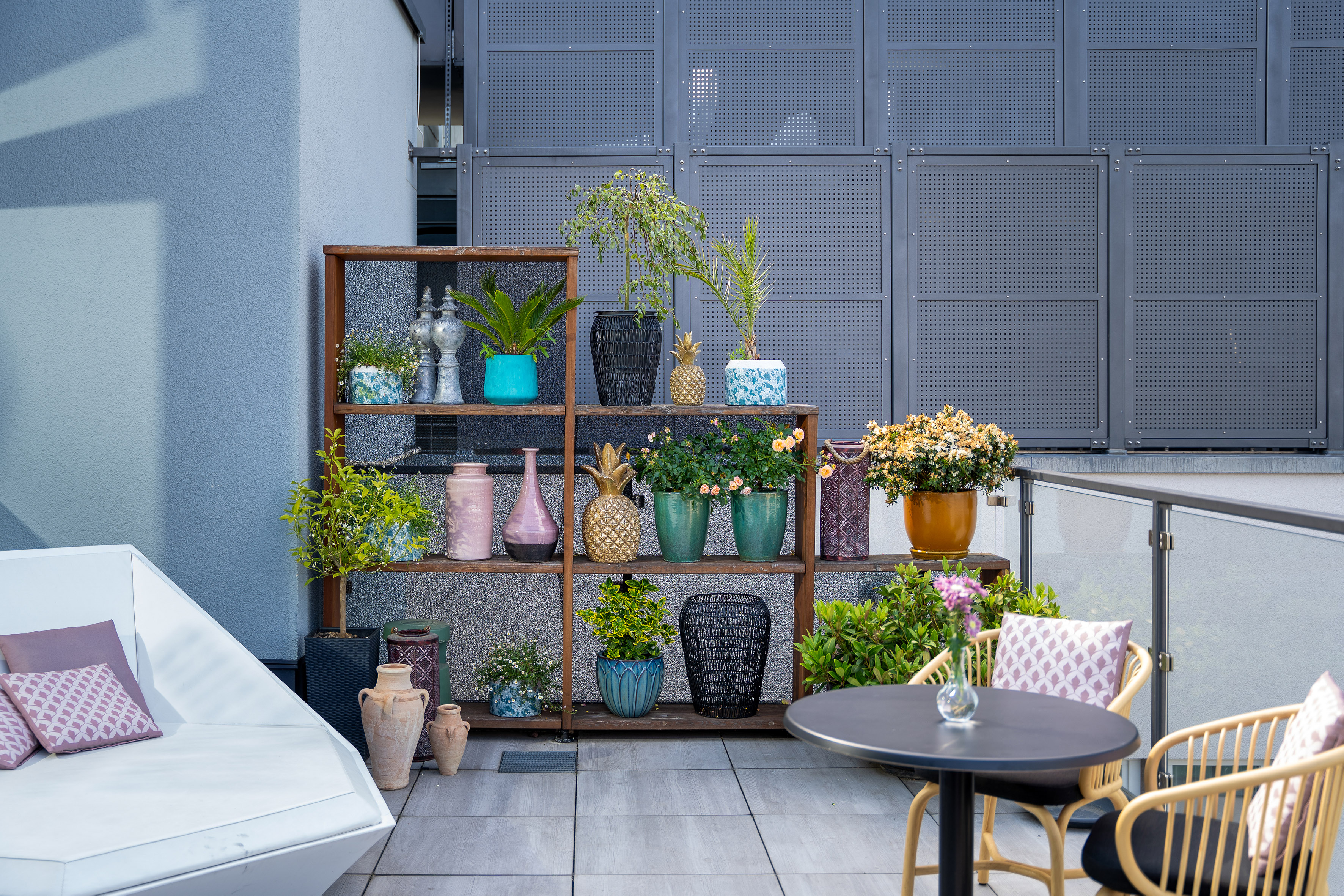 Modern balcony with diverse potted plants, decorative shelf, and outdoor seating.
