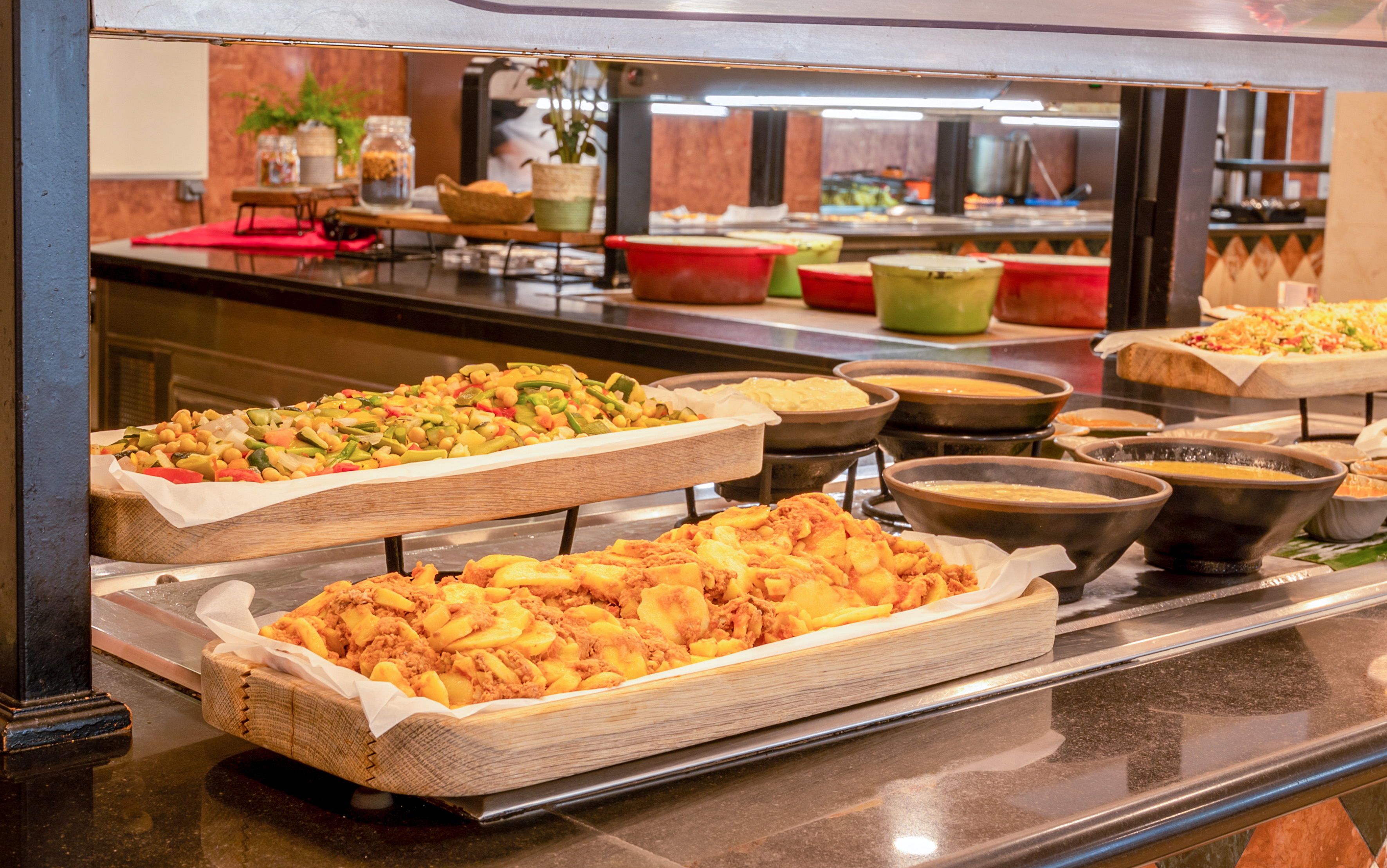 Hot buffet spread featuring fresh vegetables, seasoned potatoes, and warm soups.