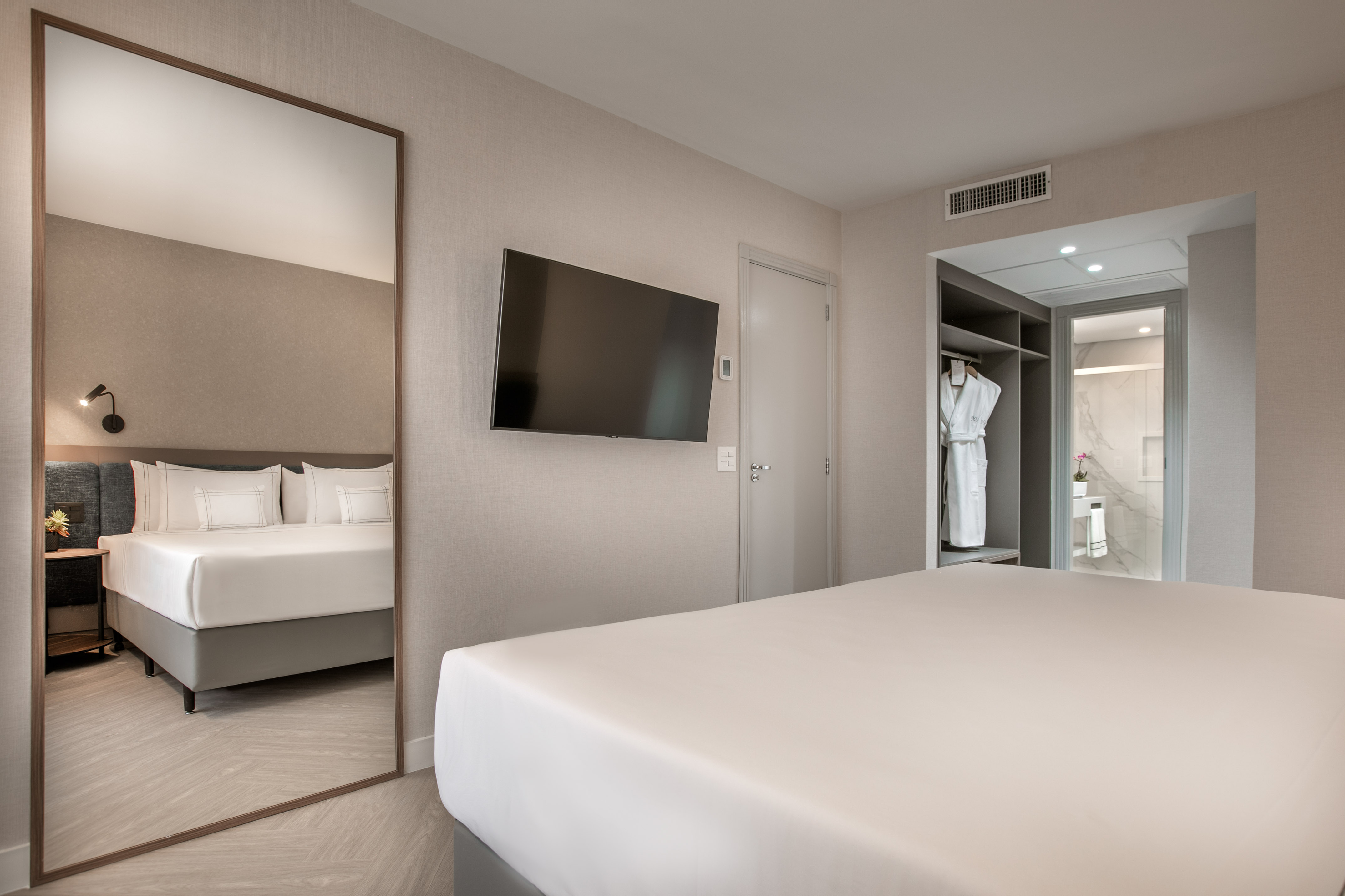 Modern hotel bedroom with bed, wall TV, large mirror, and view into bathroom.