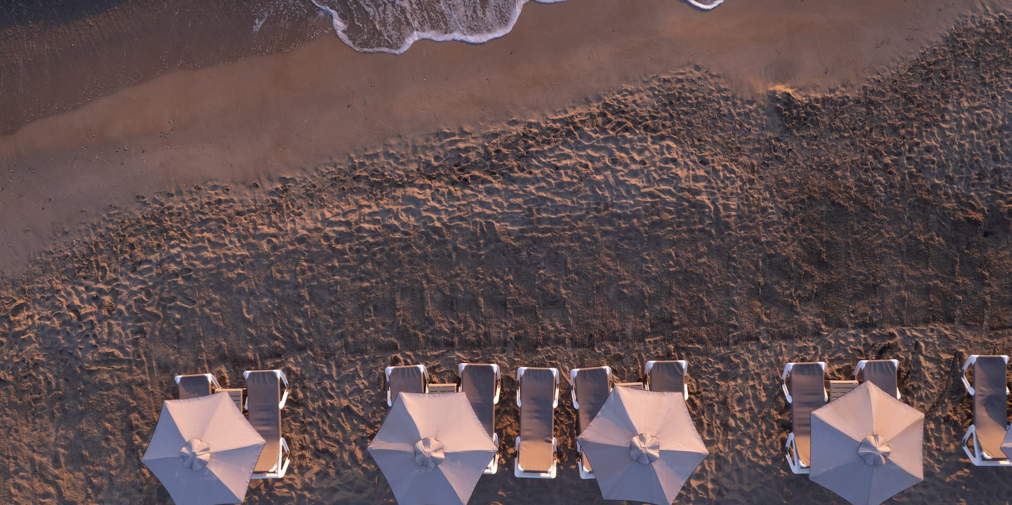 Aerial beach view: rows of grey umbrellas, sun loungers, ocean waves.