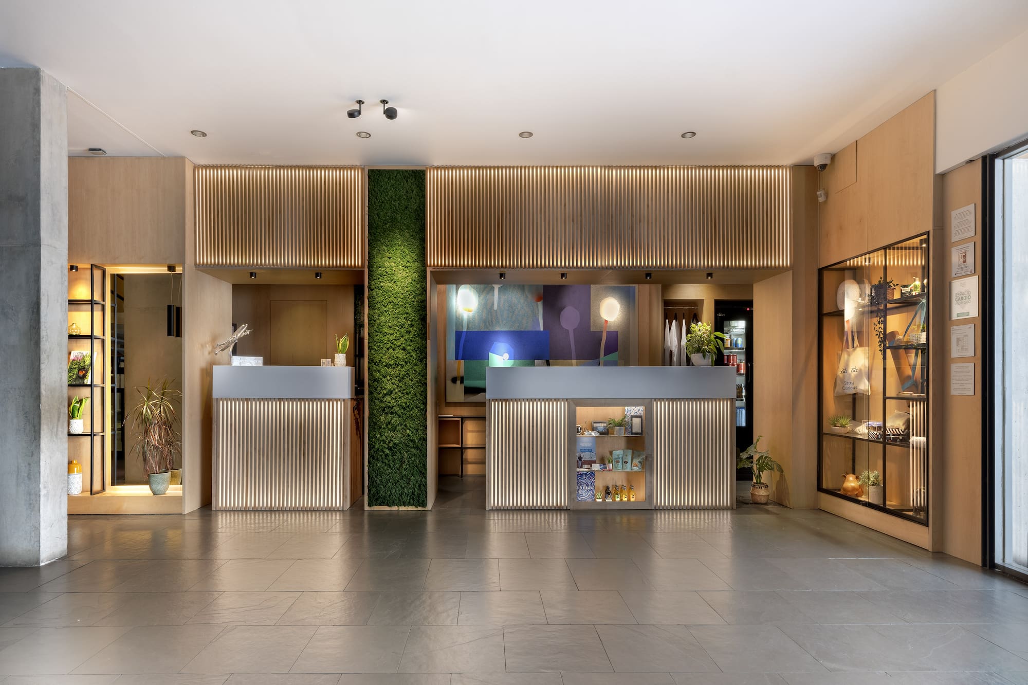 Modern hotel lobby with illuminated reception desks, green moss wall, and wood accents.