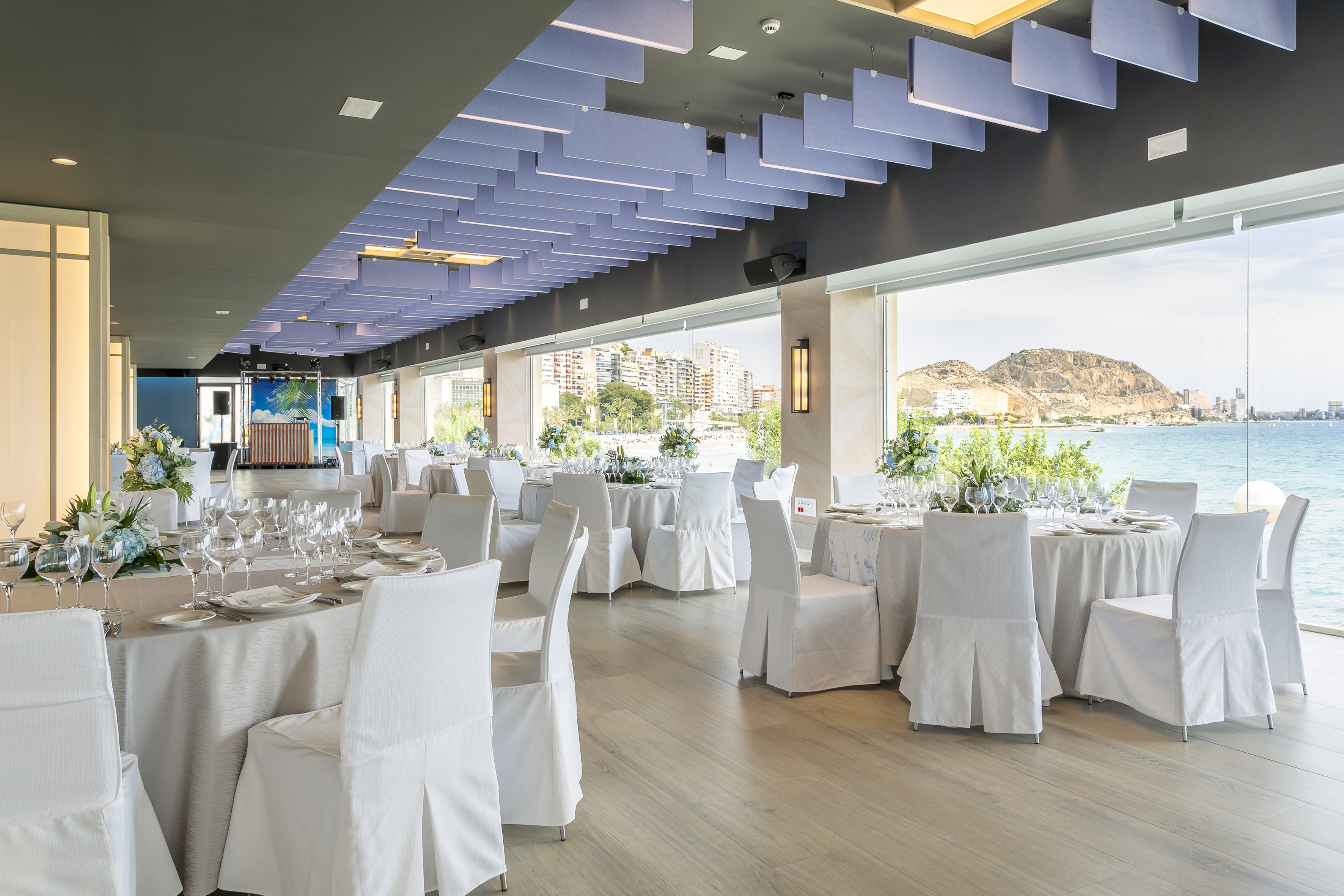 Seafront banquet hall with set tables, white chairs, and modern decor.