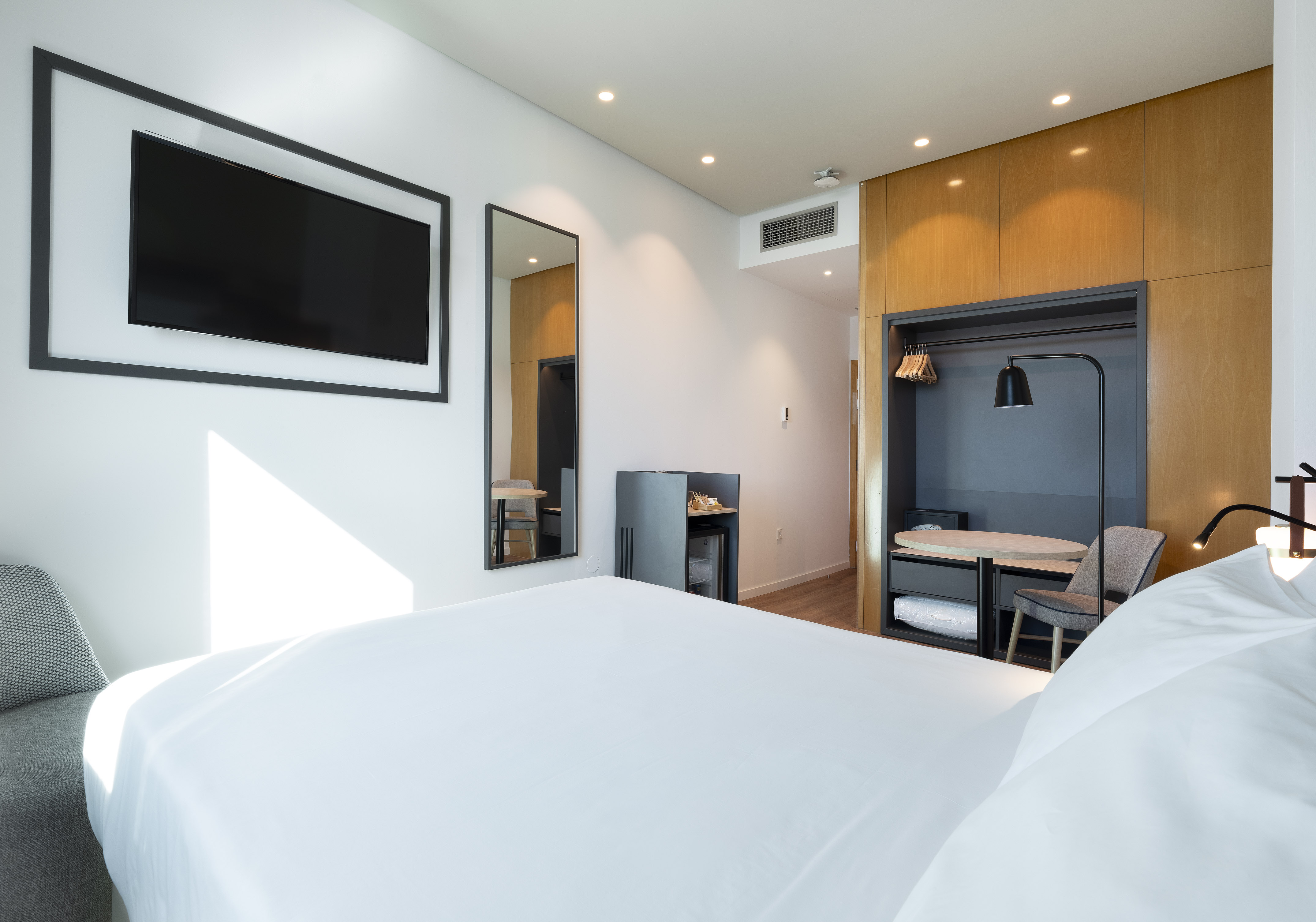 Bright modern hotel room with white bed, flat-screen TV, and wood-paneled closet.
