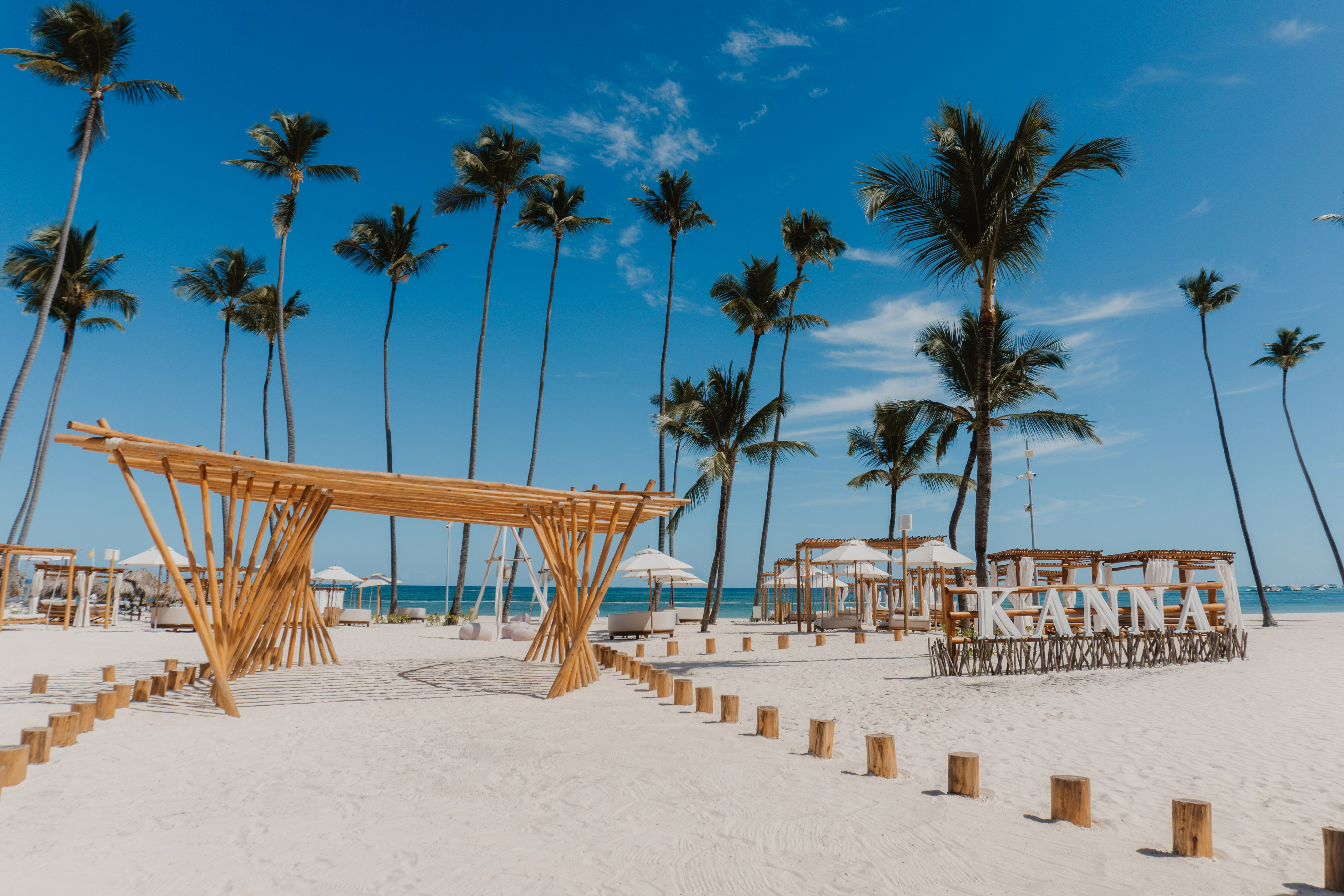 Kanna tropical beach: white sand, tall palm trees, bamboo arch, blue ocean.
