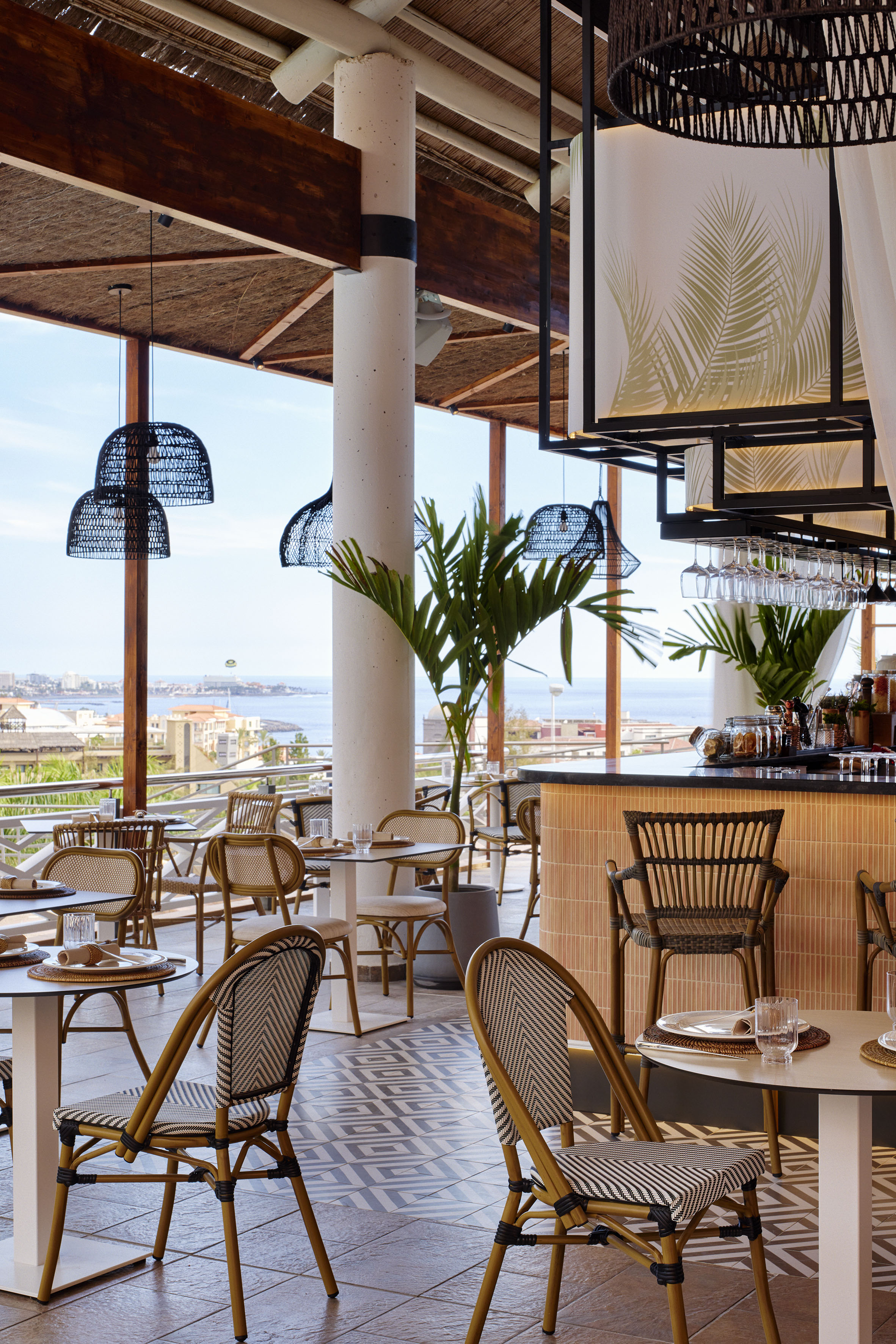 Coastal restaurant terrace with ocean view, rattan chairs, and tropical decor.
