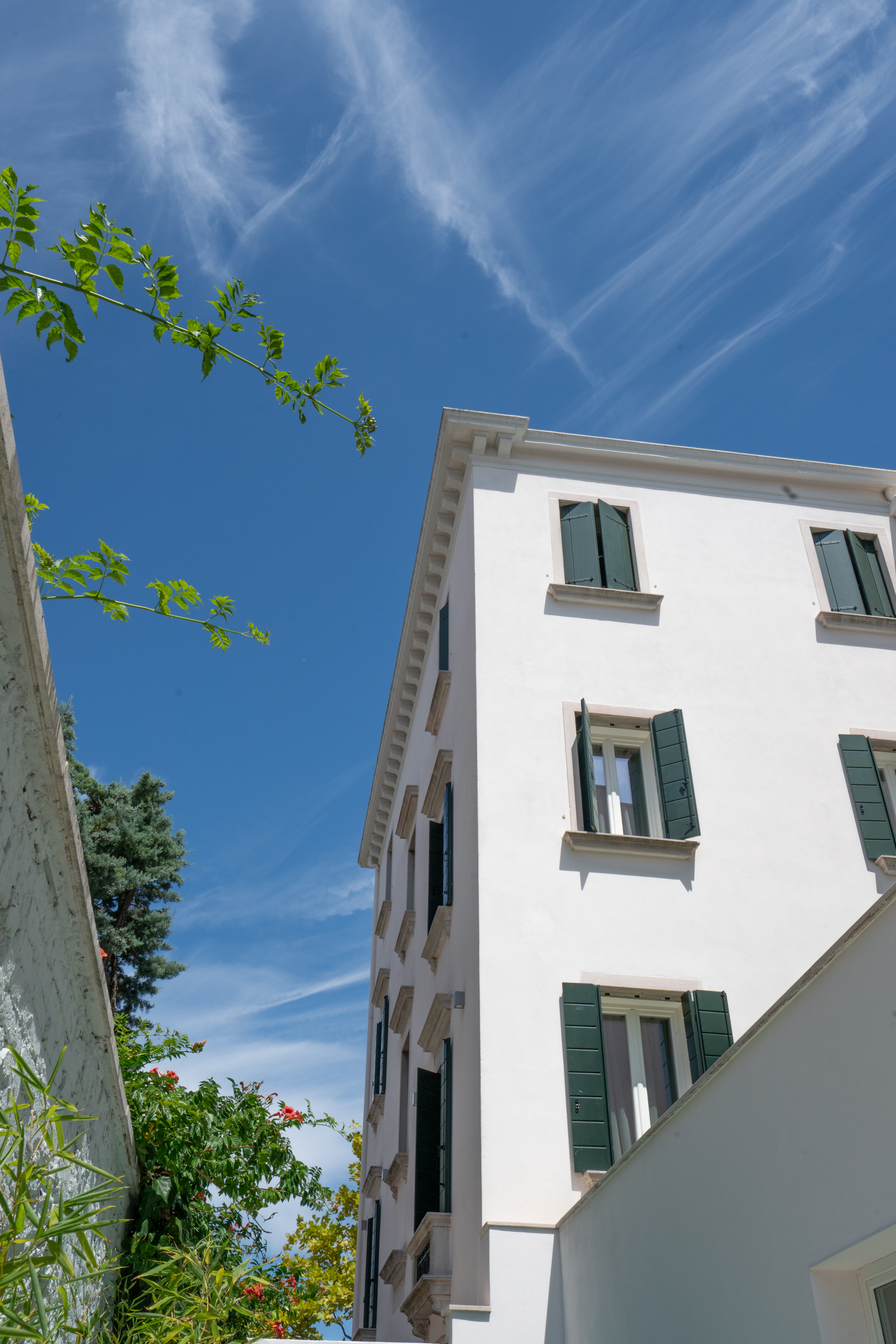 White building with green shutters, clear blue sky, and green foliage.