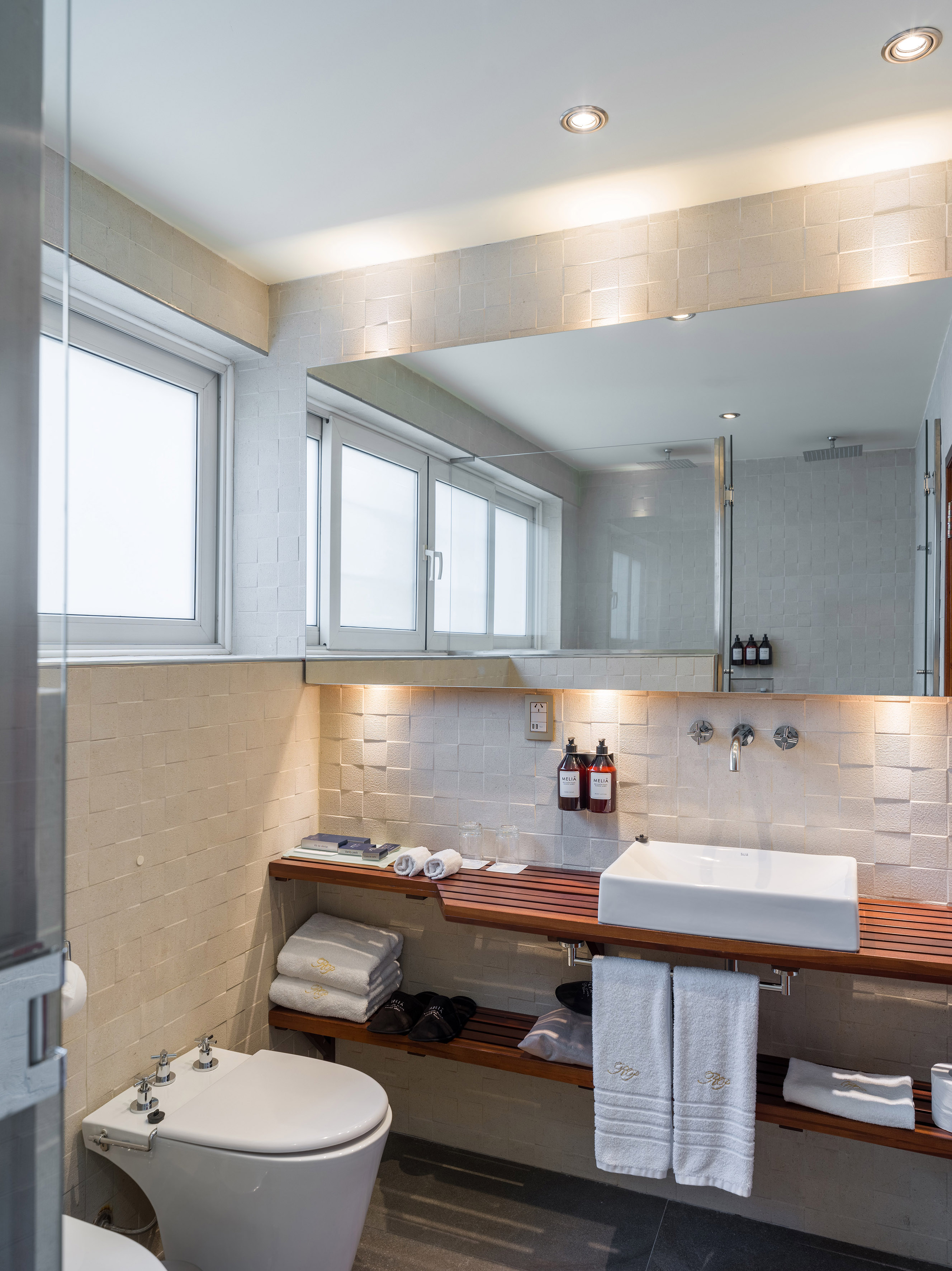 Modern hotel bathroom with white sink, wooden vanity, large mirror, and shower.