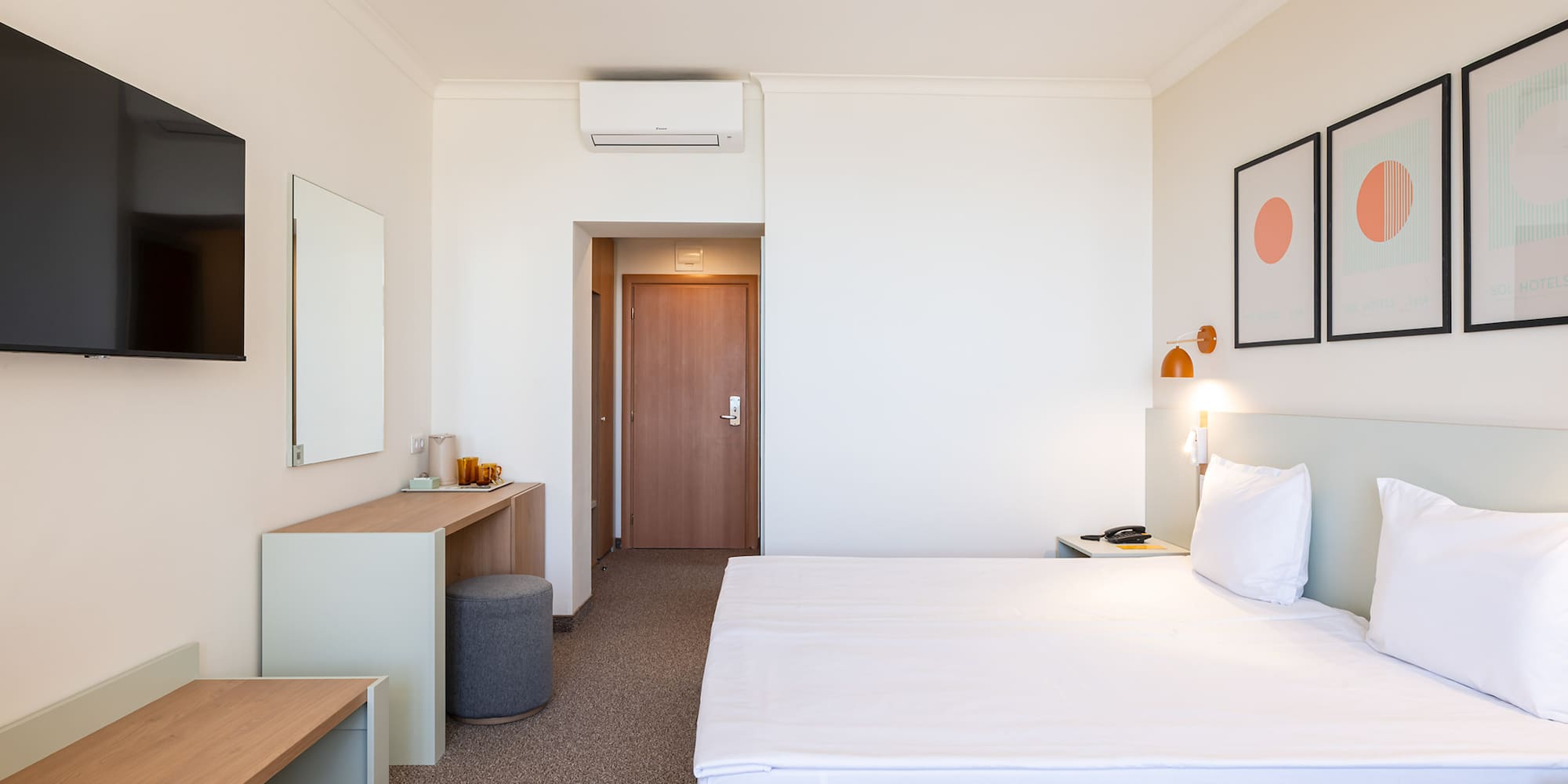 Contemporary hotel room with white bed, desk, wall-mounted TV, and artwork.