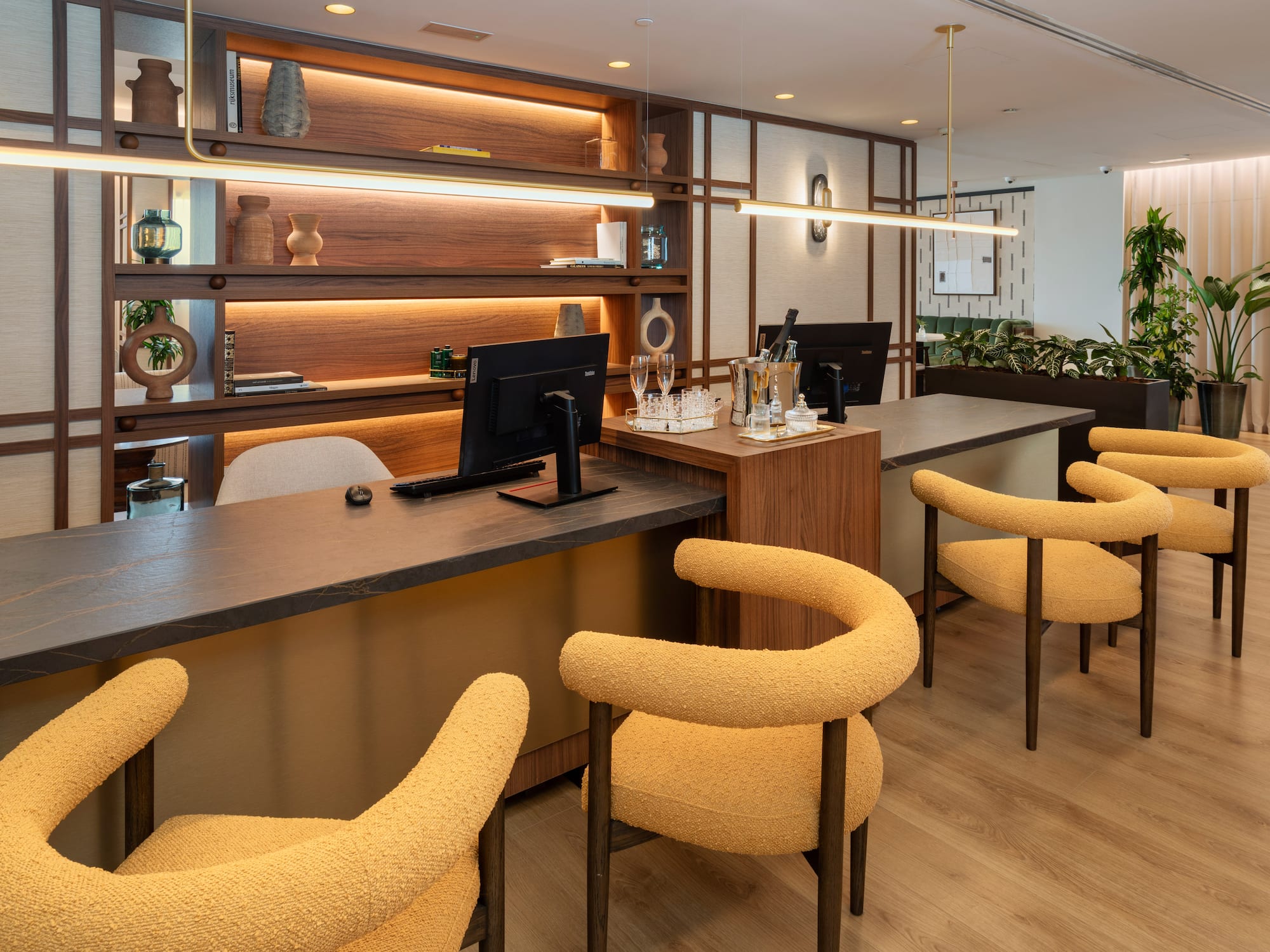 Modern hotel reception desk with yellow upholstered chairs and backlit wooden shelves.