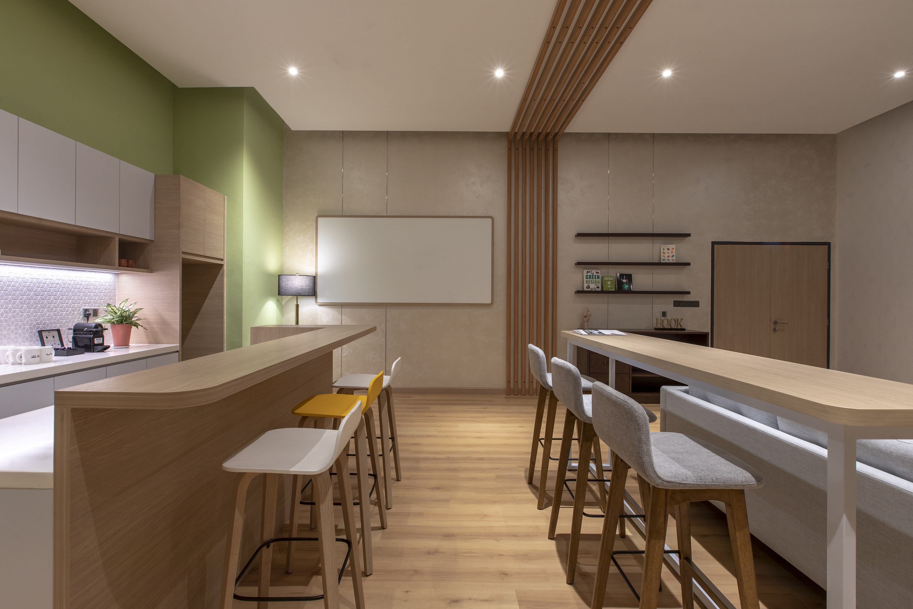 Modern office breakroom with kitchen, bar counter, green wall, and lounge seating.