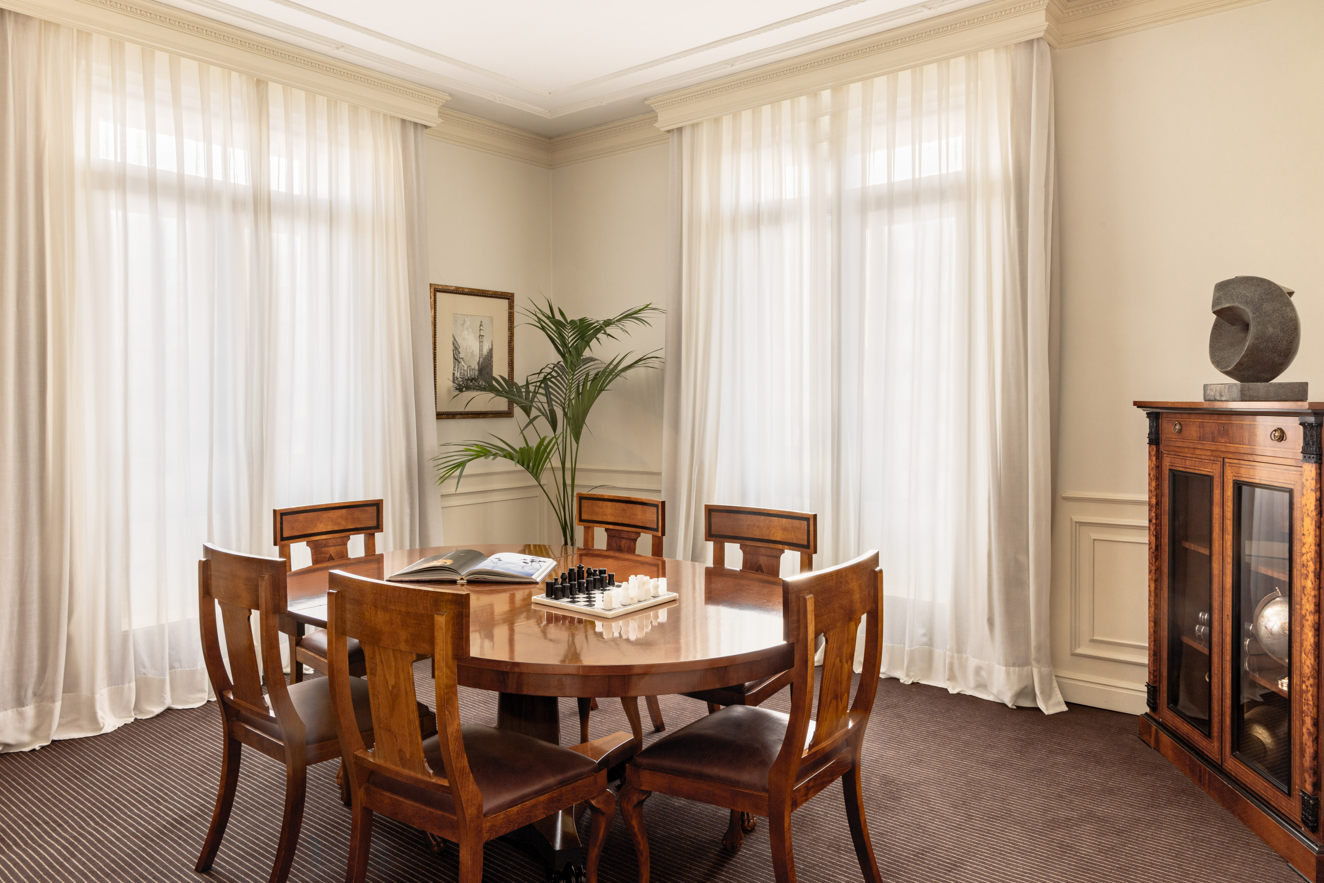 Classic room with round wooden table, chess set, chairs, and sheer curtains.