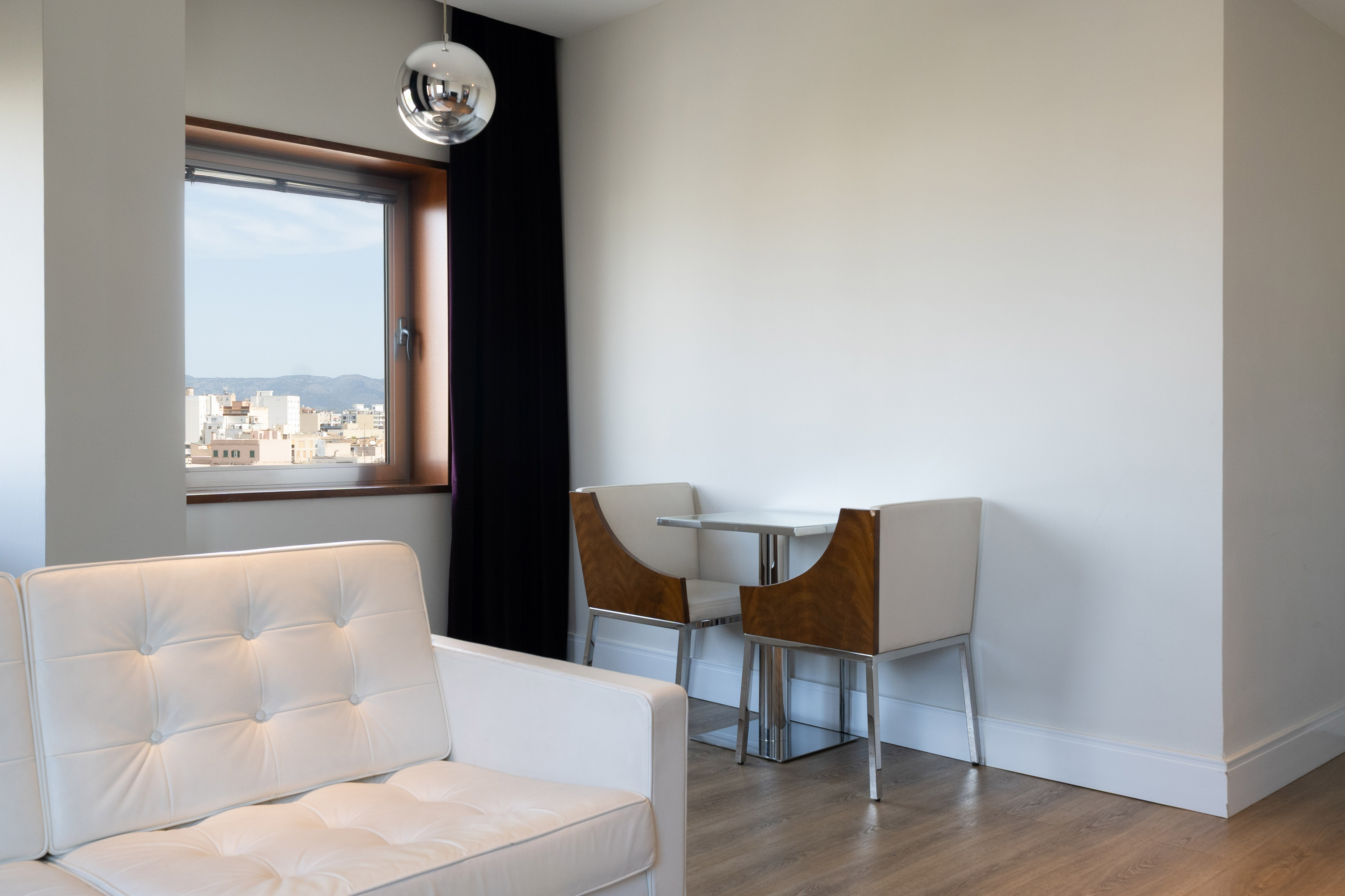 Bright modern living space with white sofa, dining set, and city view.