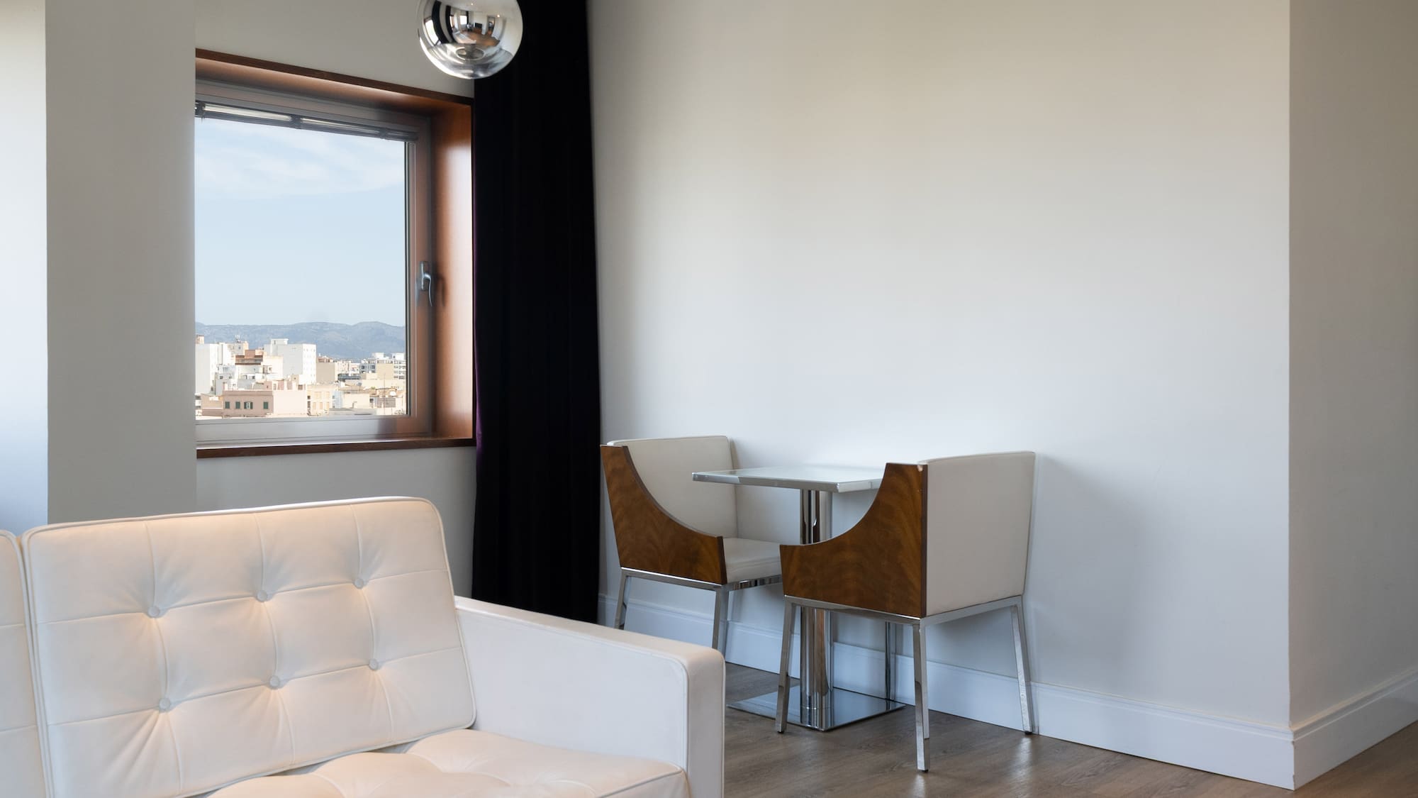 Bright modern living space with white sofa, dining set, and city view.