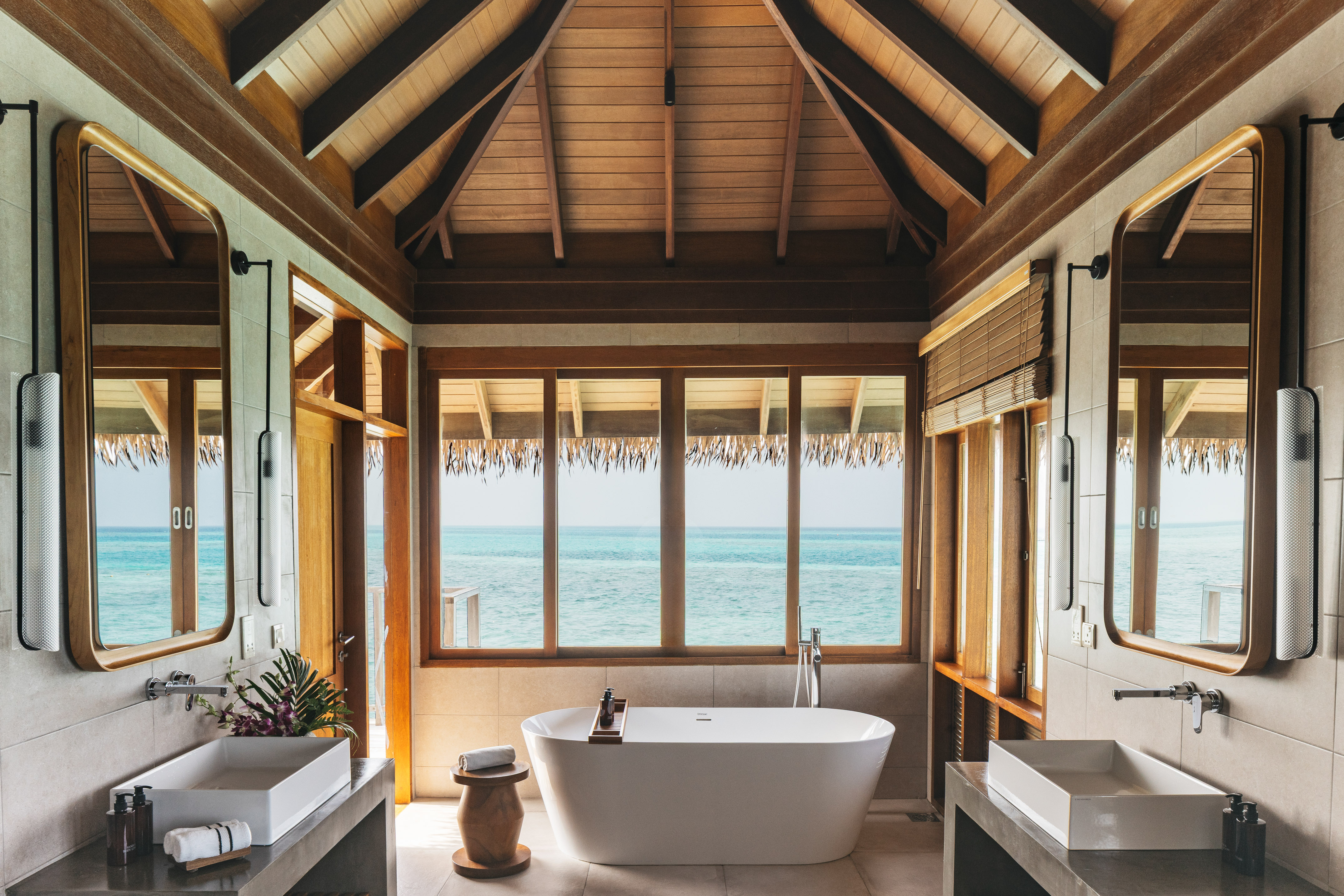 Luxury overwater bathroom with ocean view, freestanding tub, dual sinks.