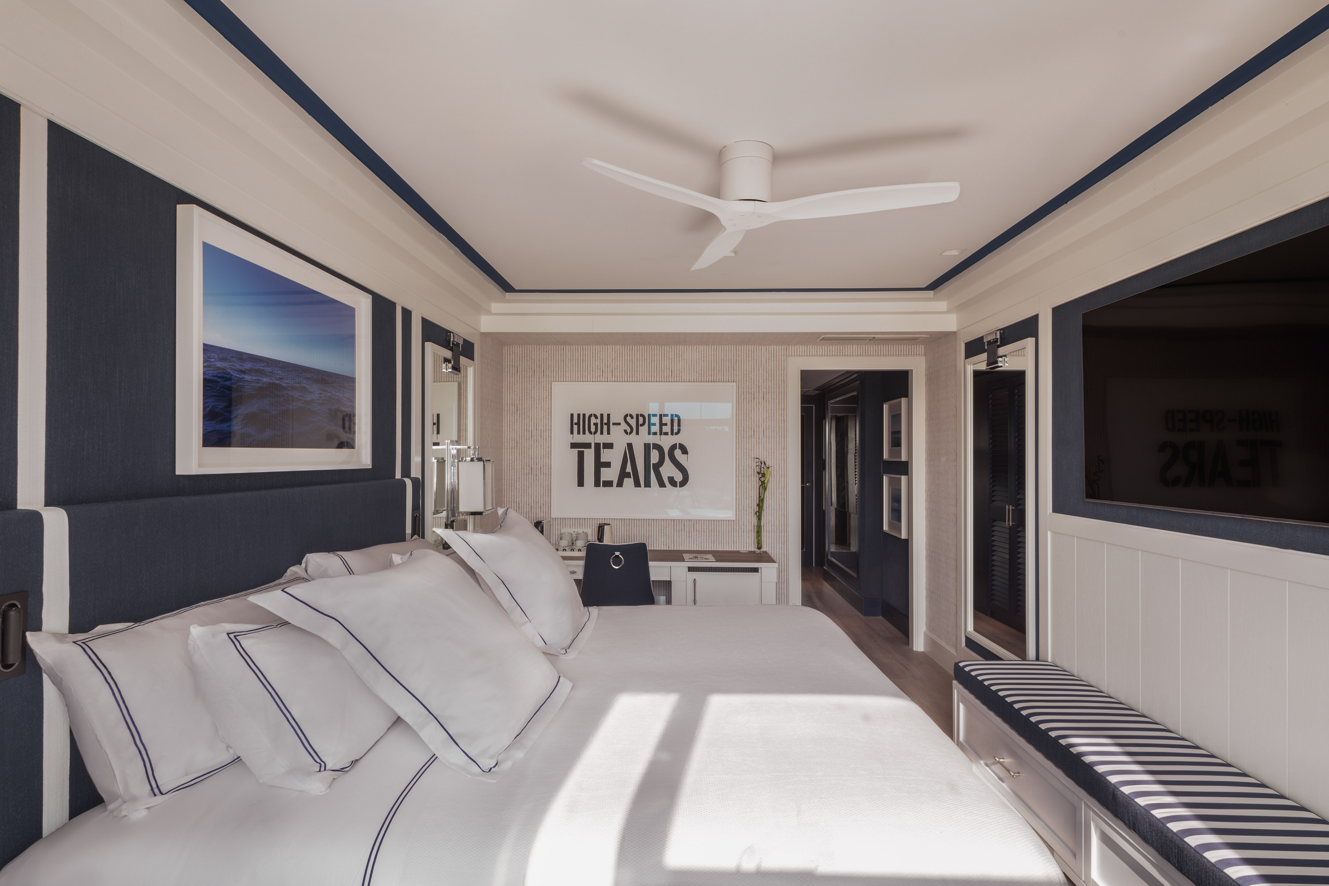 Coastal bedroom with navy accents, large white bed, modern fan, and wall art.