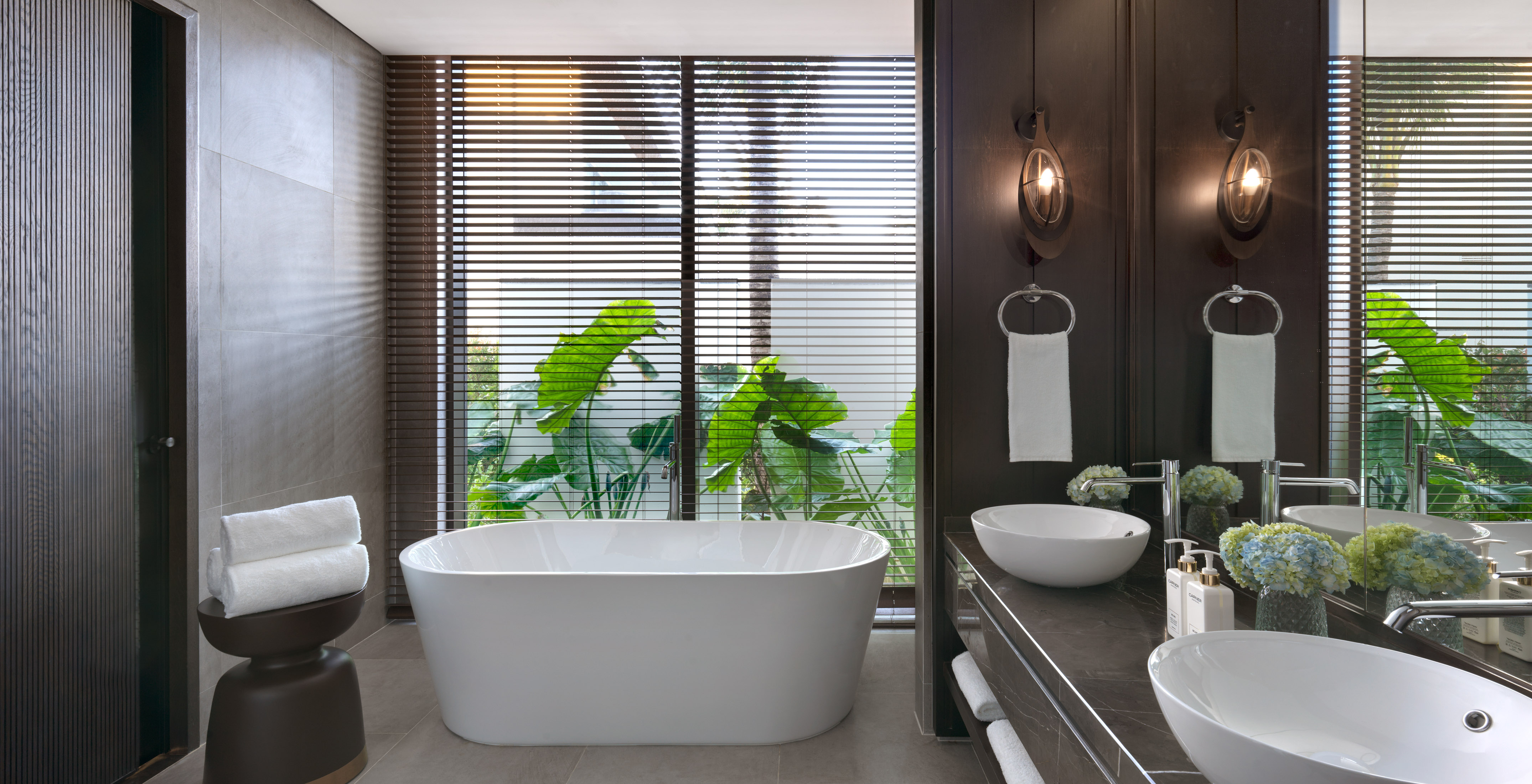 Modern bathroom with freestanding tub, double vanity, and tropical view.