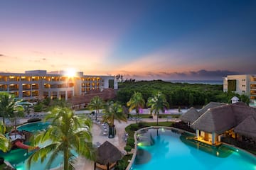 a pool with palm trees and a building with a beach and a sunset